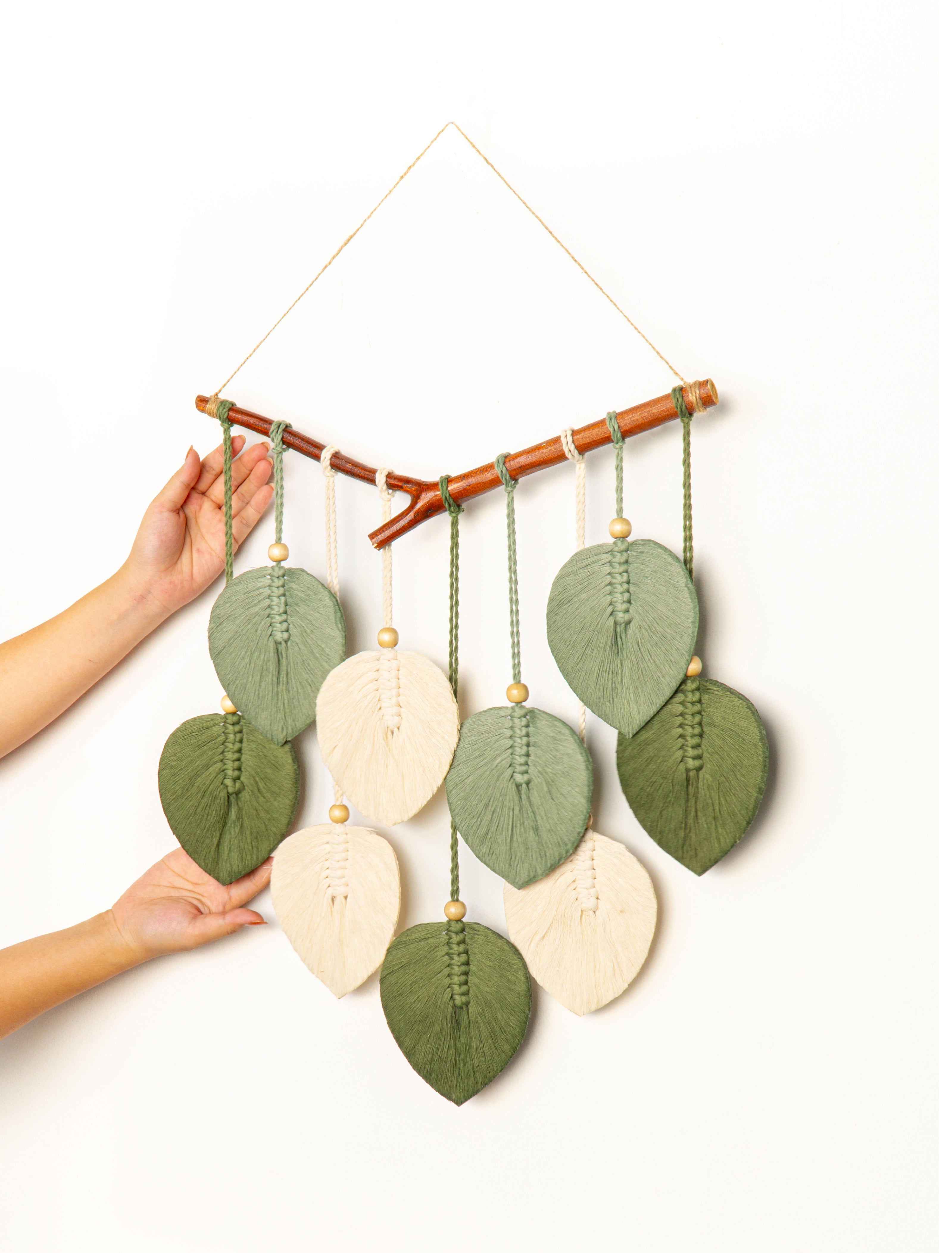 Handmade leaf-shaped wall hanging with a person's hand holding it on a white background