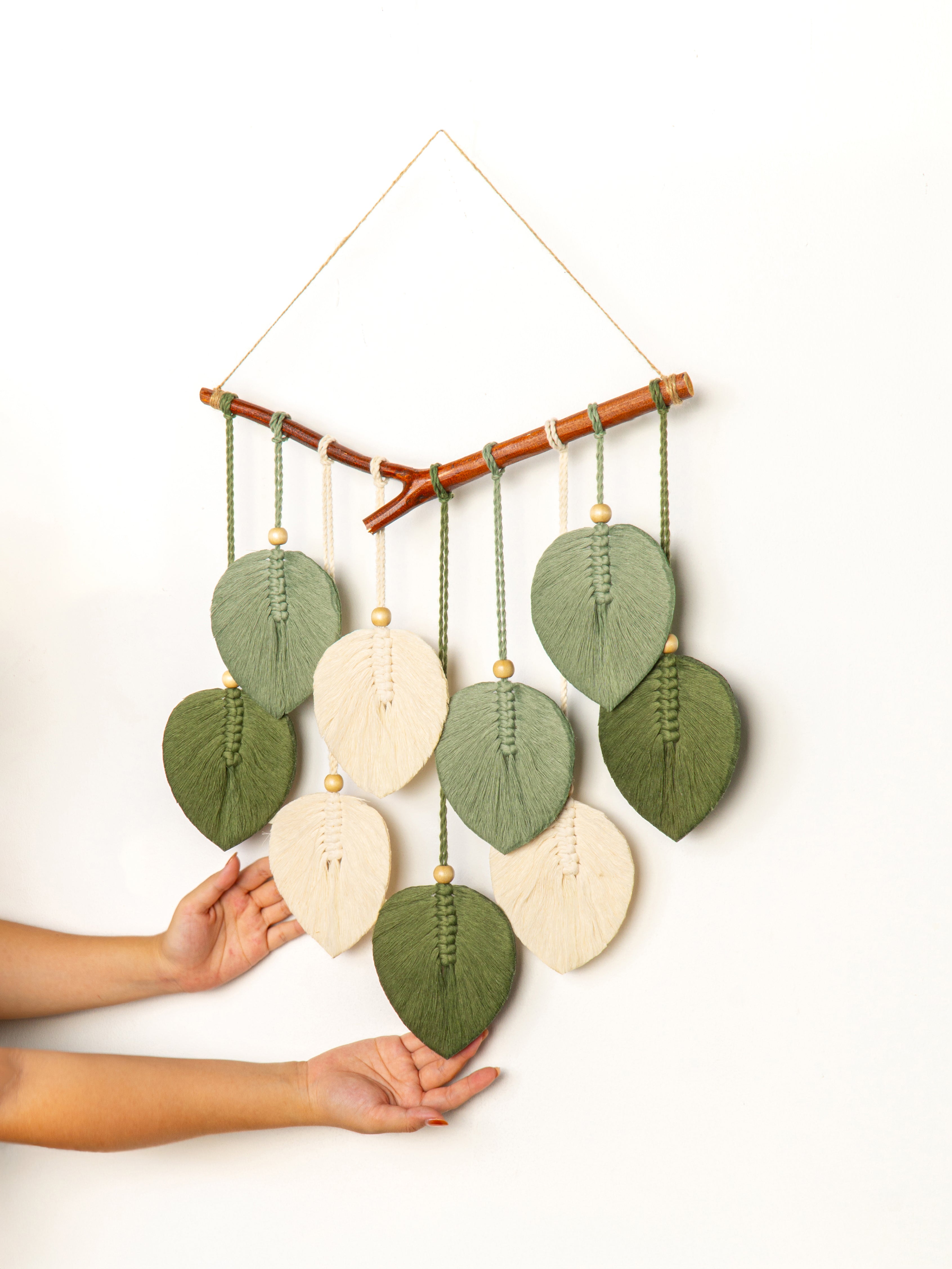 Handmade leaf-shaped wall hanging with a bamboo stick on a white background