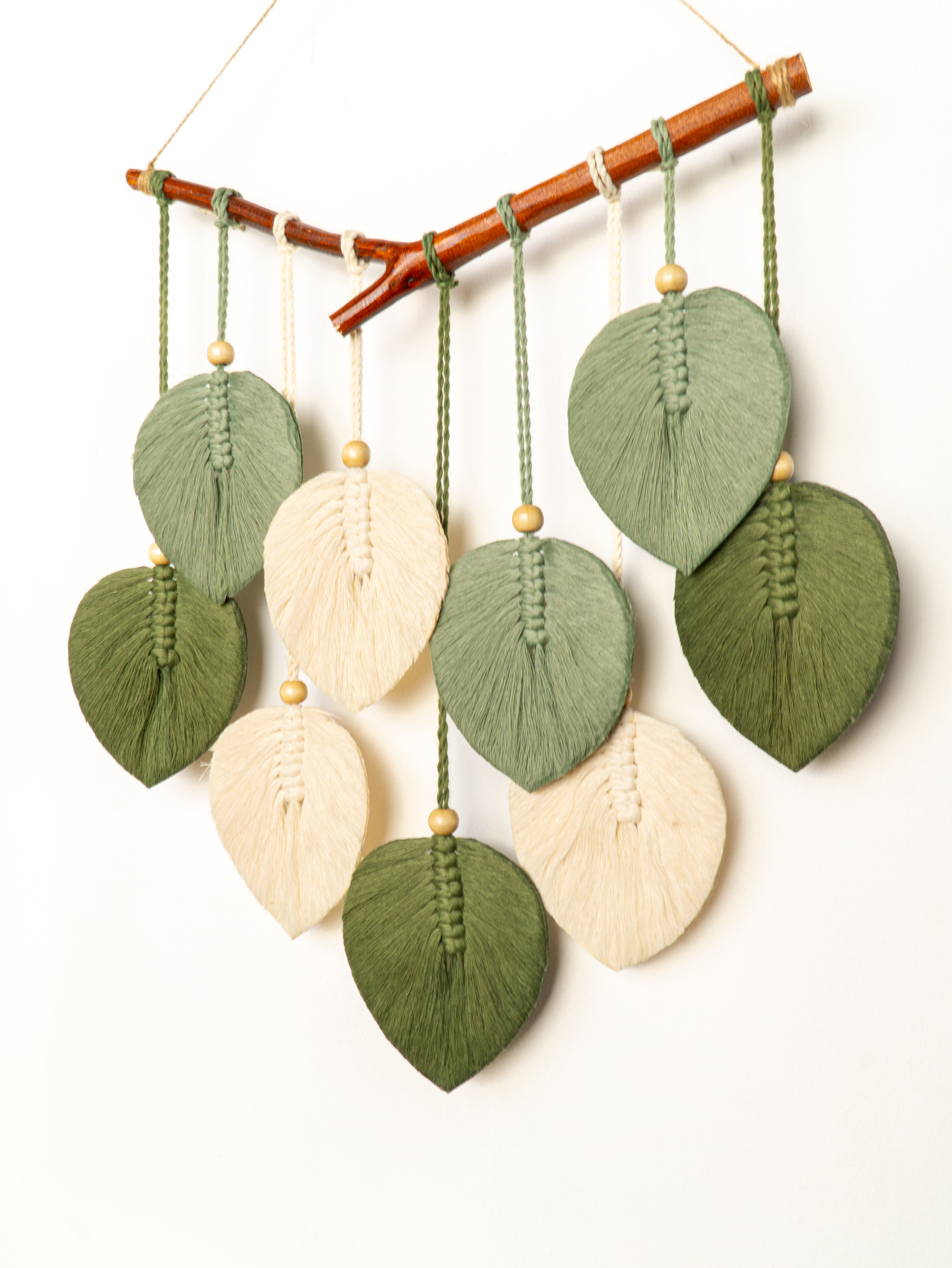 Decorative wall hanging with leaf-shaped fabric pieces in green and beige on a white background.