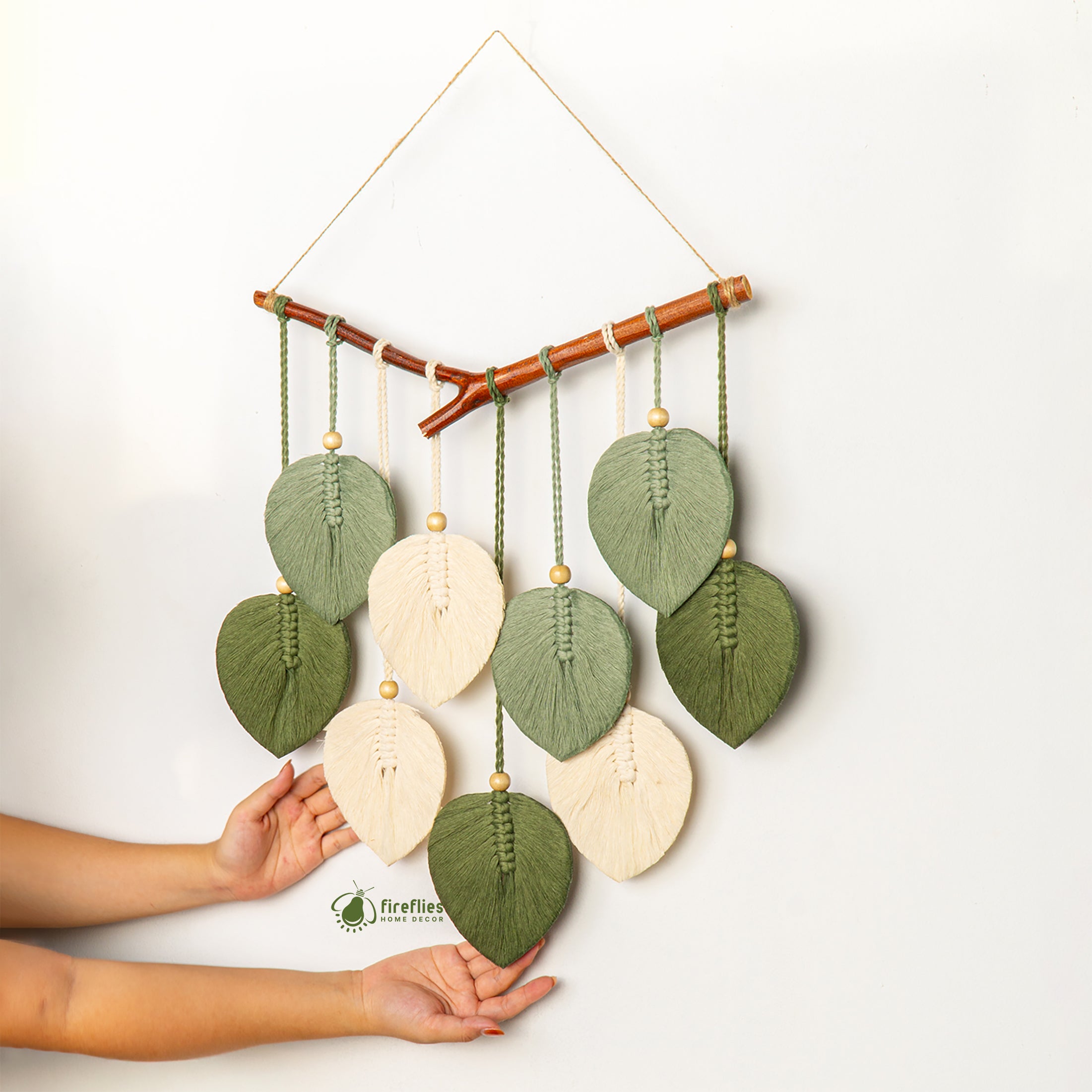 Handmade wall hanging with leaf-shaped green and beige elements on a white background