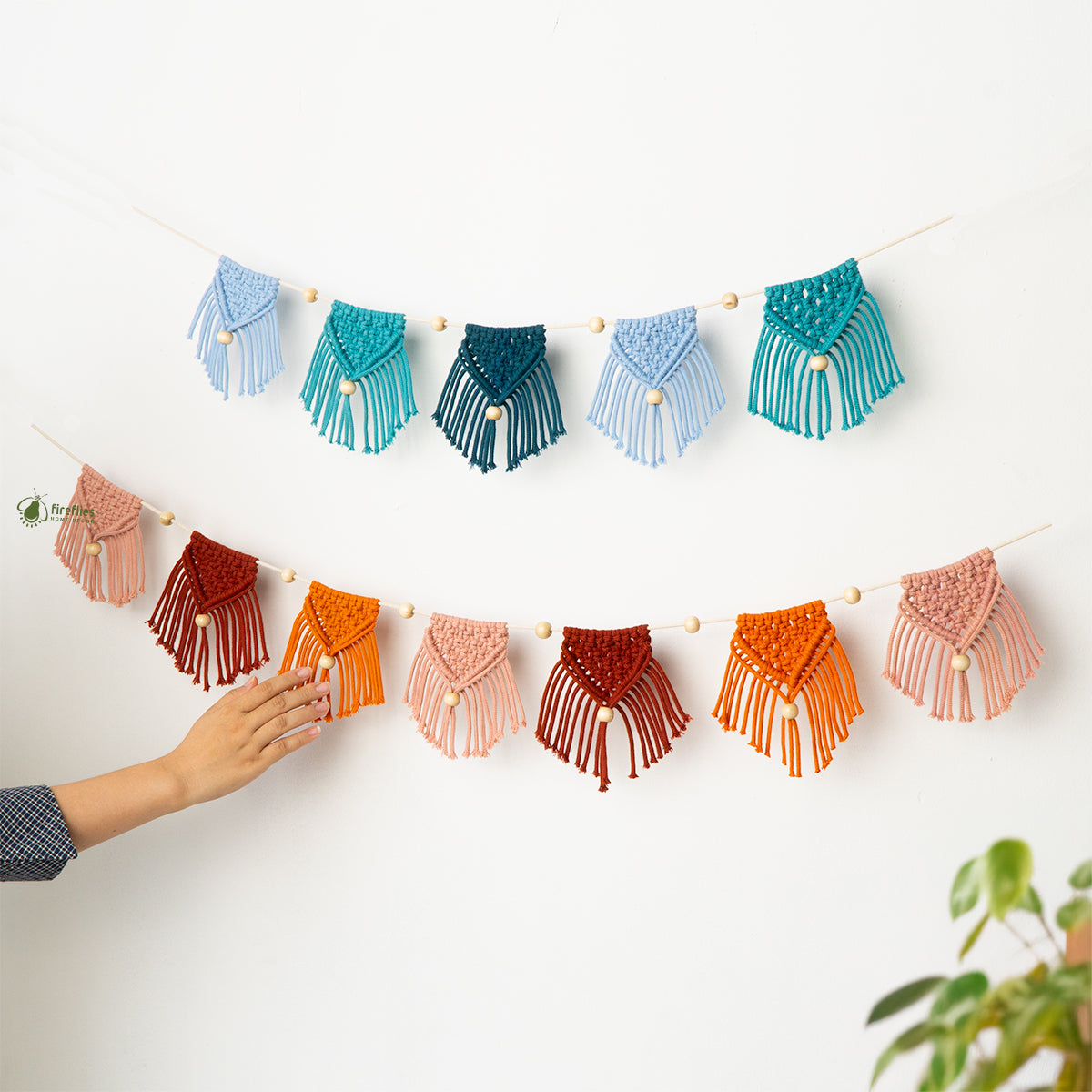 Colorful macrame wall hanging with a hand touching it on a white background