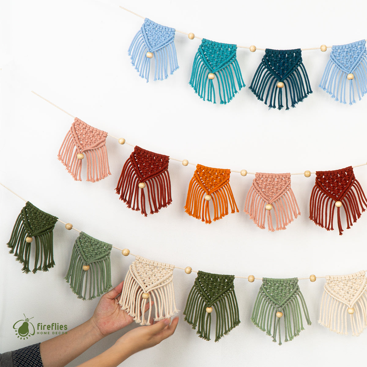 Colorful macrame wall hanging with a hand holding one of the pieces against a white background.