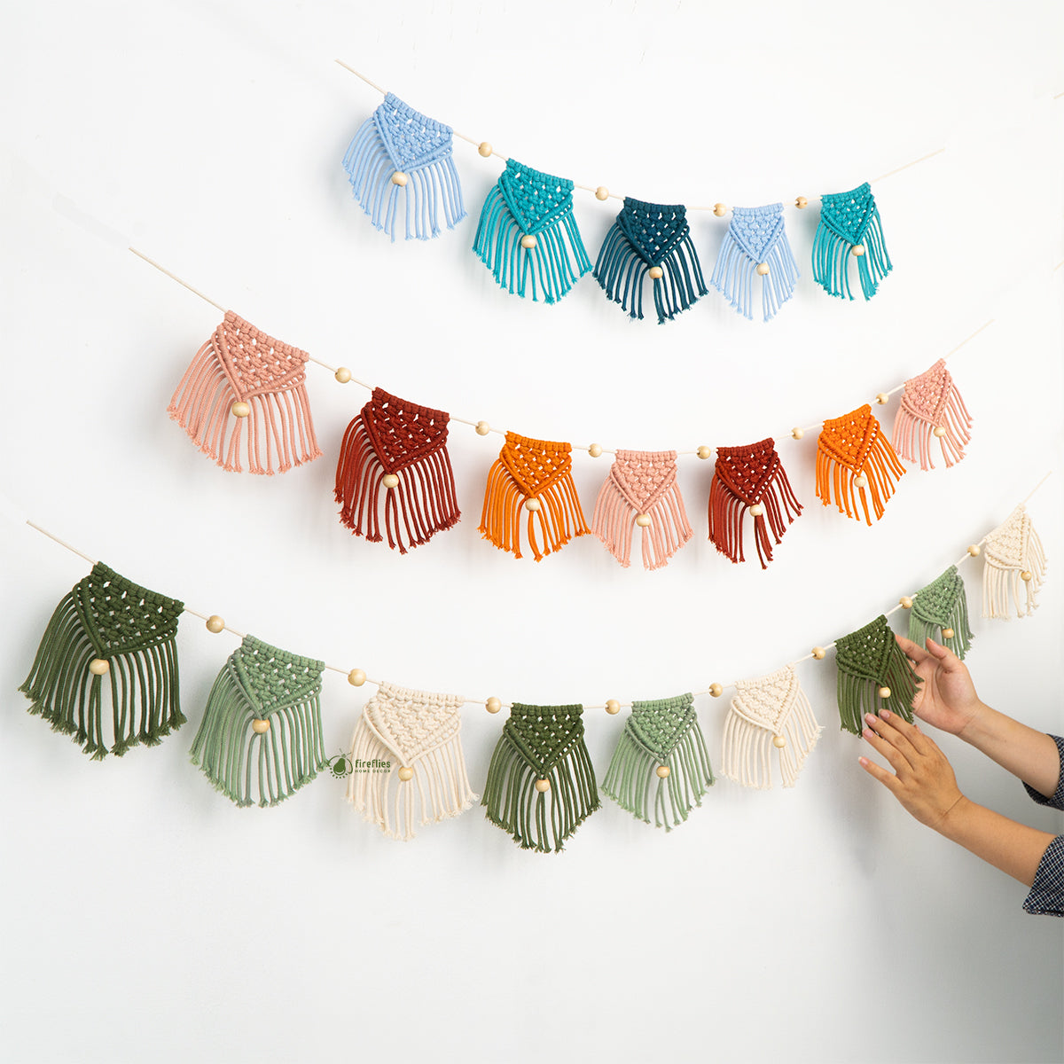 Colorful macrame wall hanging with a hand reaching to touch it on a white background