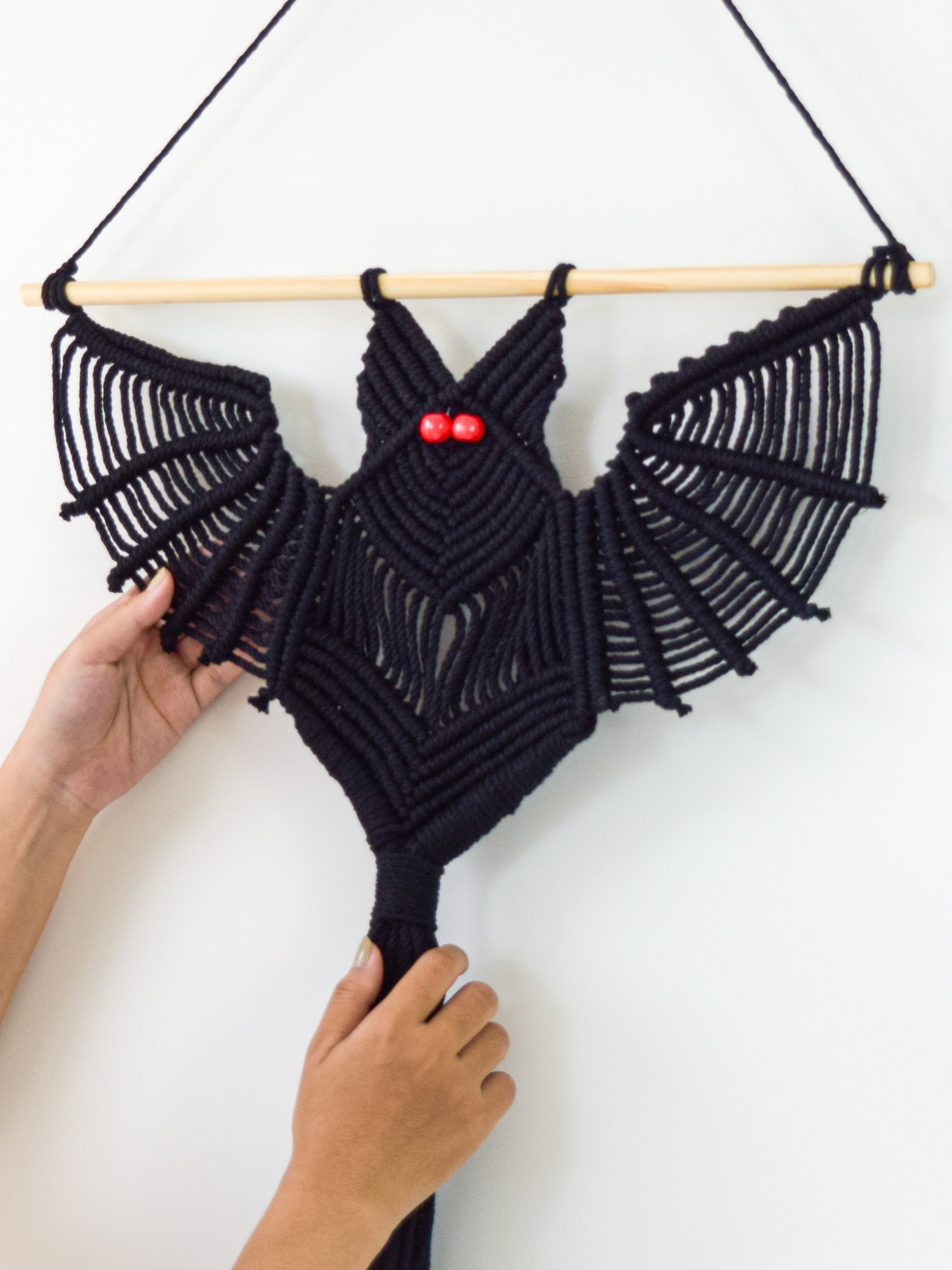 Close-up of hand-knotted black cotton cord bat header with glowing red bead eye details.   