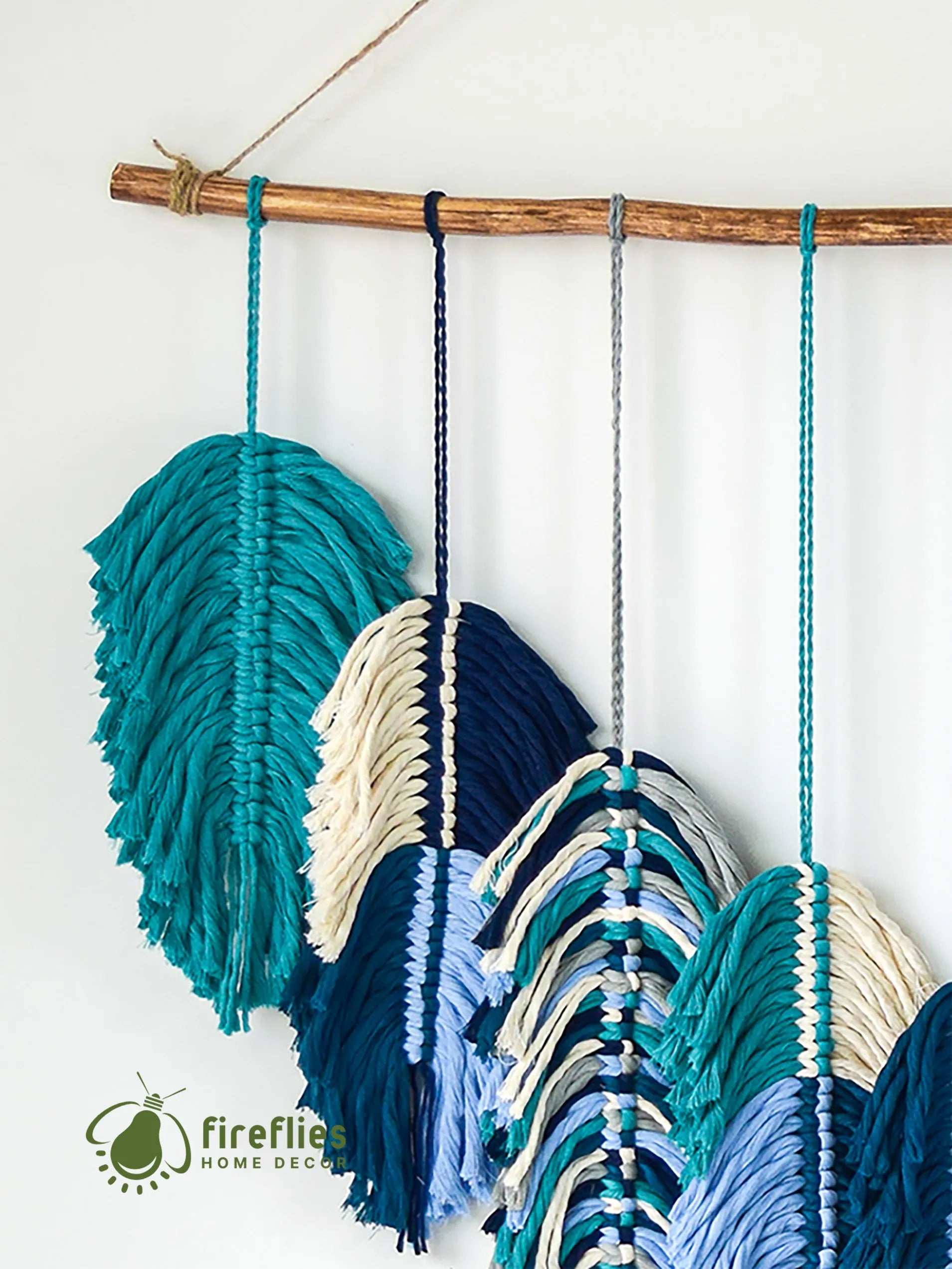 Decorative wall hanging with colorful yarn and wooden stick on a white background, featuring the Fireflies Home Decor logo.