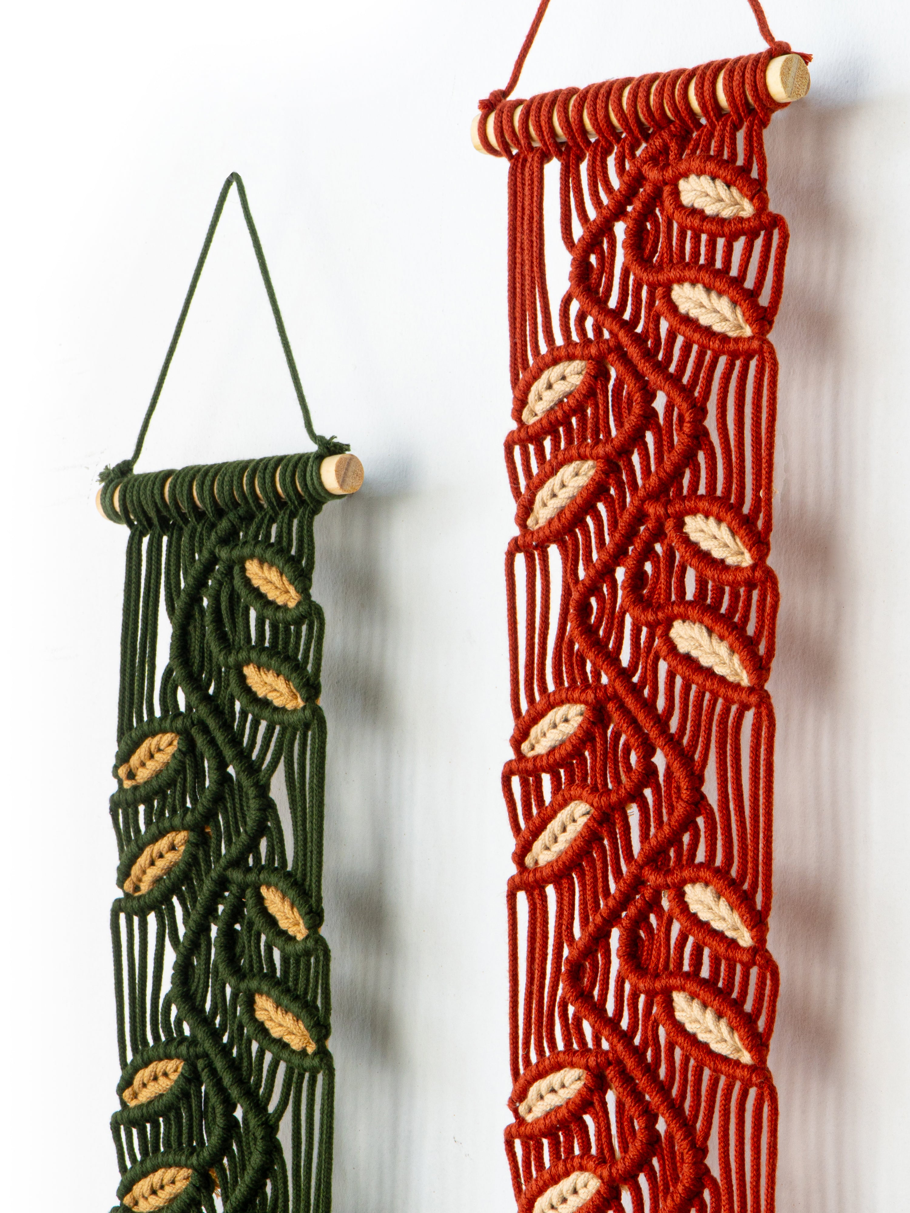Two macrame wall hangings, one green and one red, against a white background.