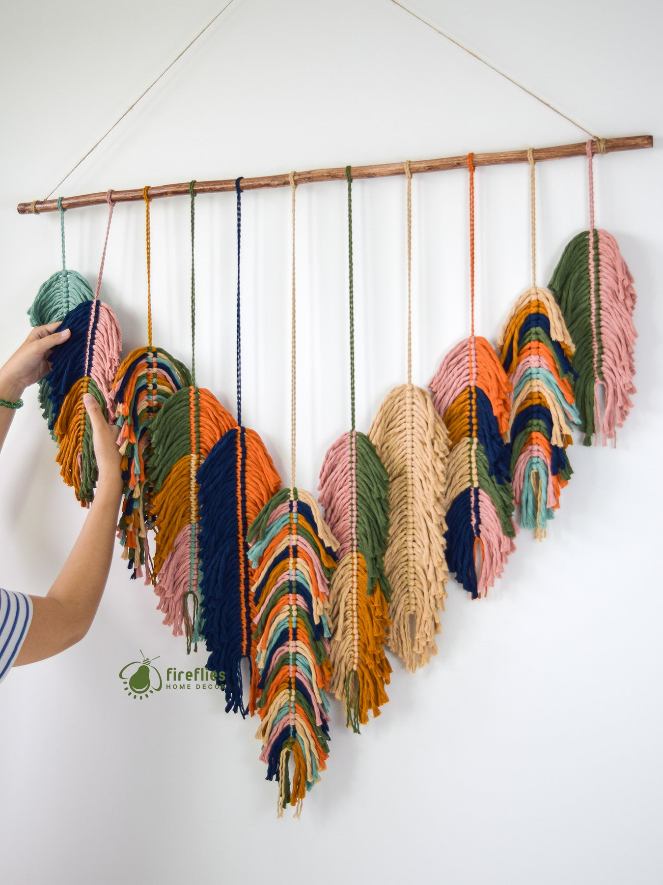 Colorful yarn skeins hanging on a wooden rod against a white wall.
