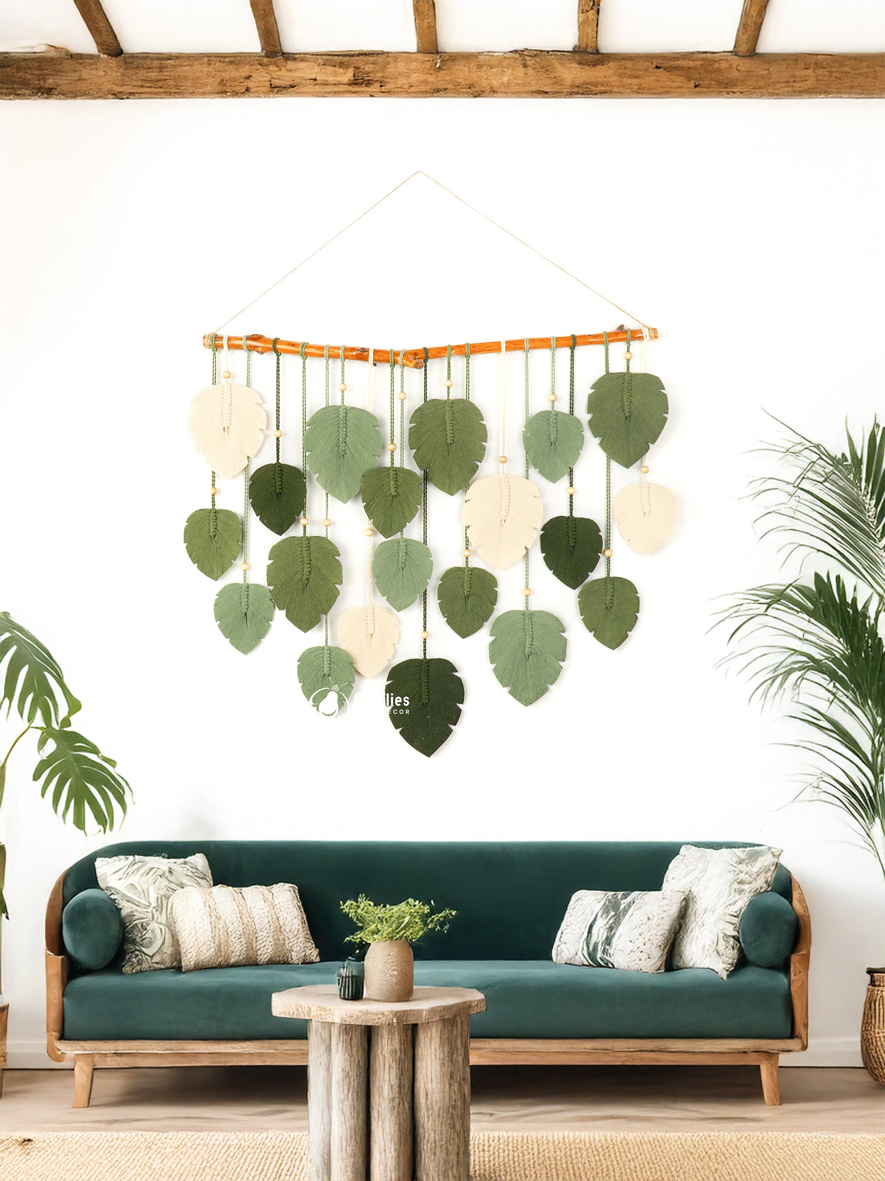 Decorative leaf mobile hanging above a green sofa in a room with plants.