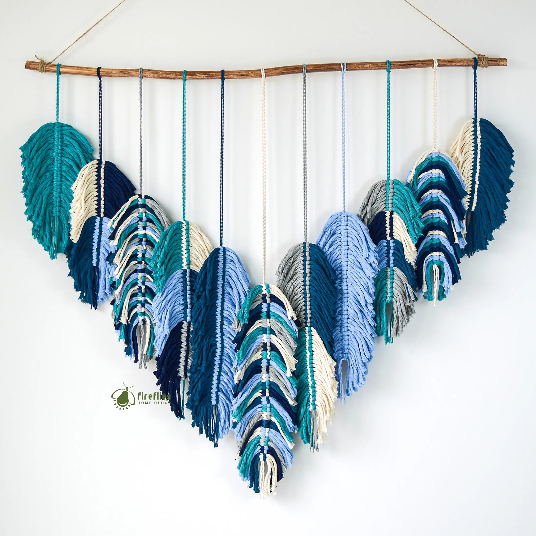 Decorative wall hanging with feather-shaped yarn pieces in blue and green on a white background.