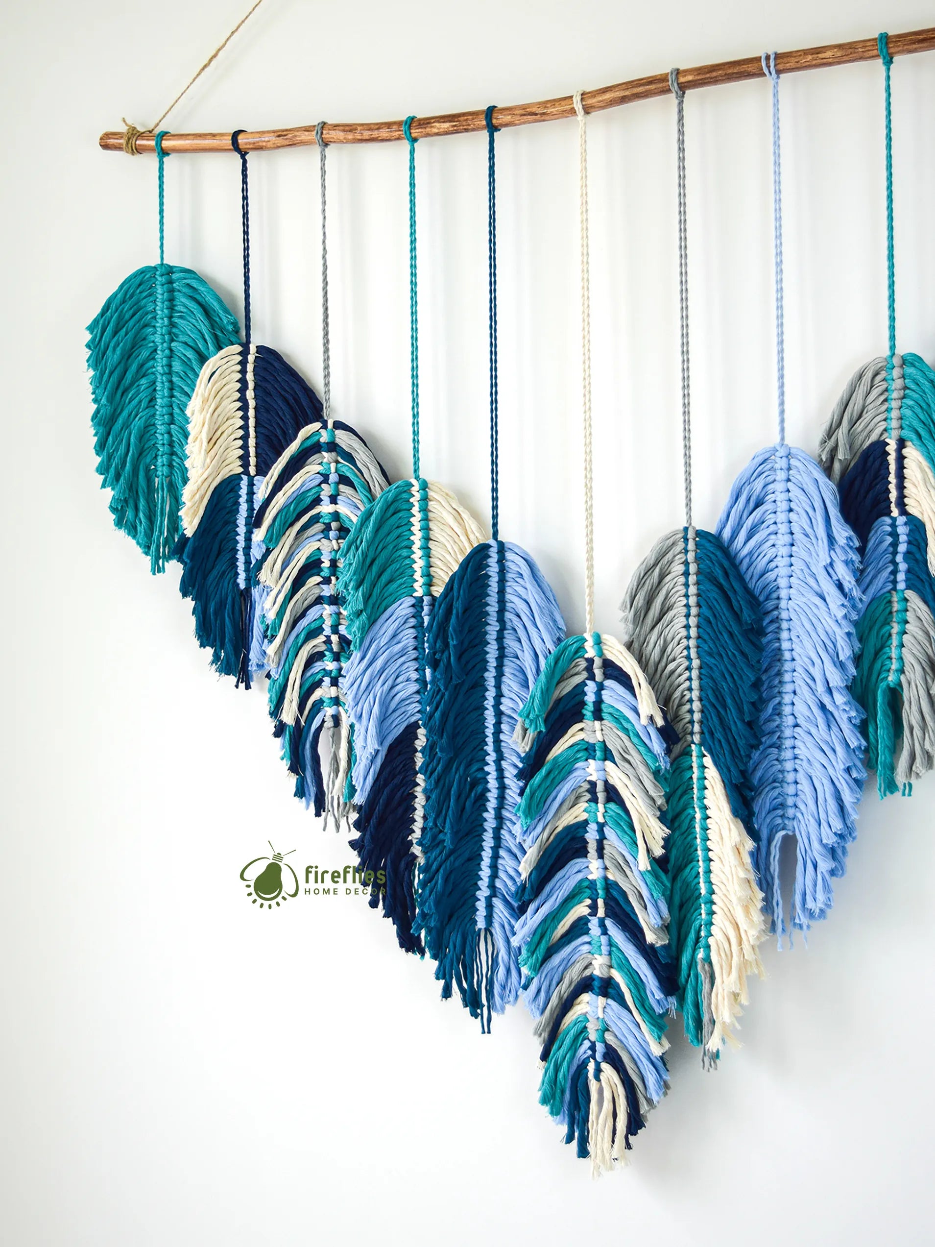 Decorative wall hanging with yarn feathers in blue and green on a white background