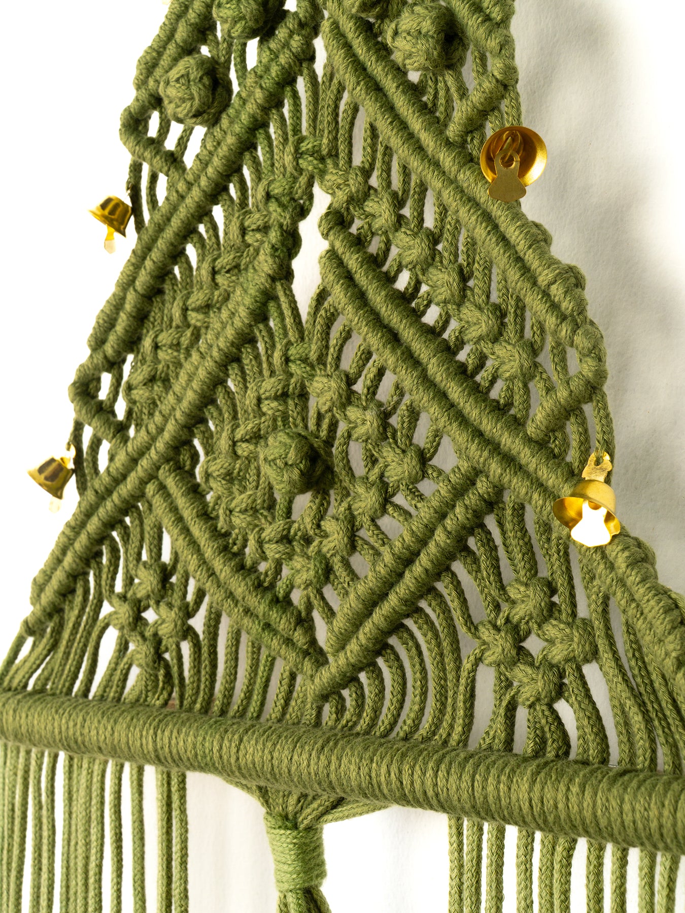 Close-up of a green macrame wall hanging with gold beads on a white background
