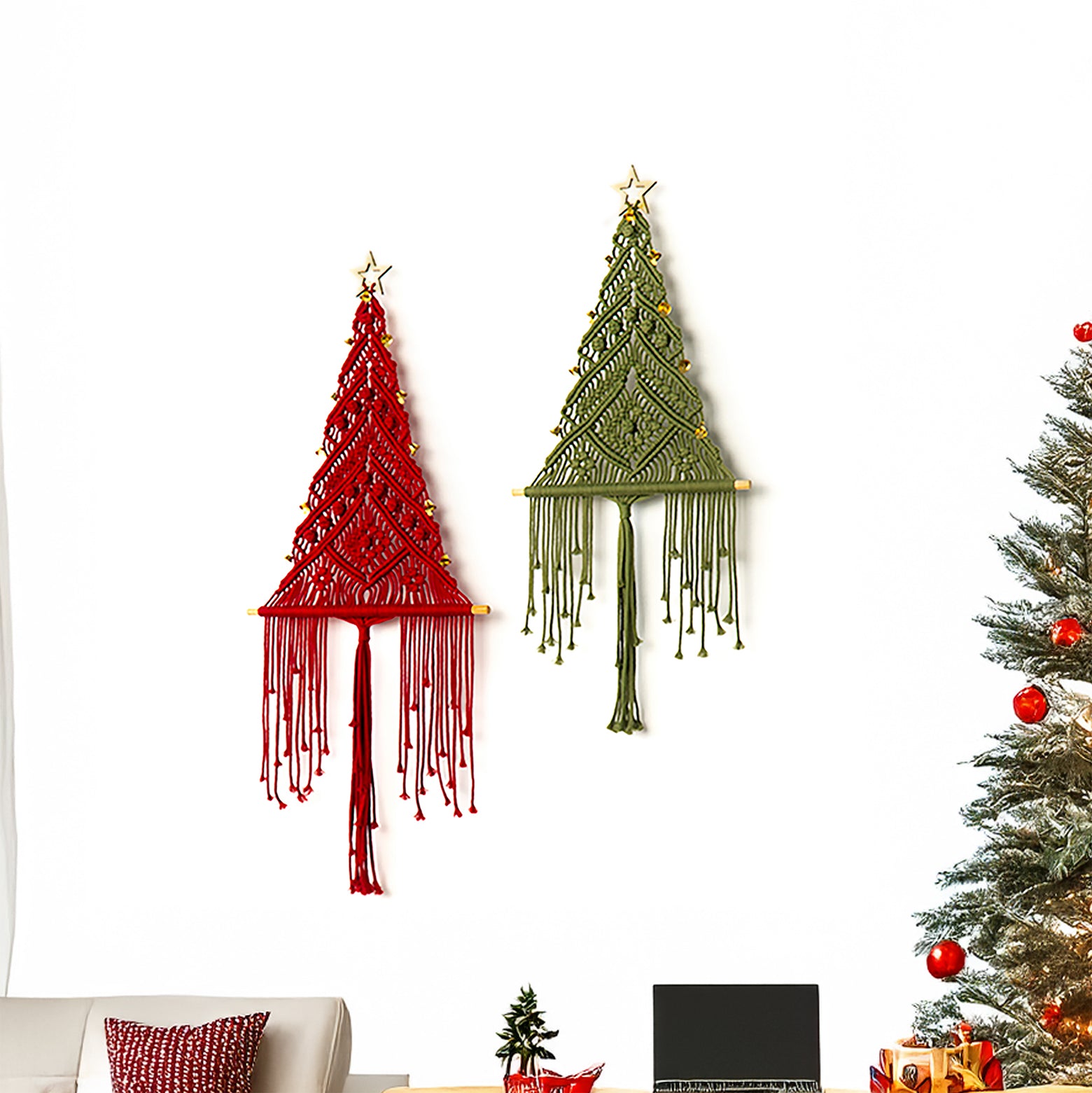 Two macrame Christmas tree wall hangings on a white wall next to a decorated Christmas tree.