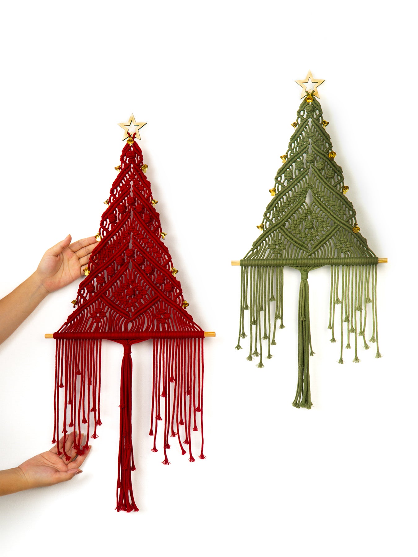 Two macrame Christmas trees, one red and one green, hanging on a white wall.