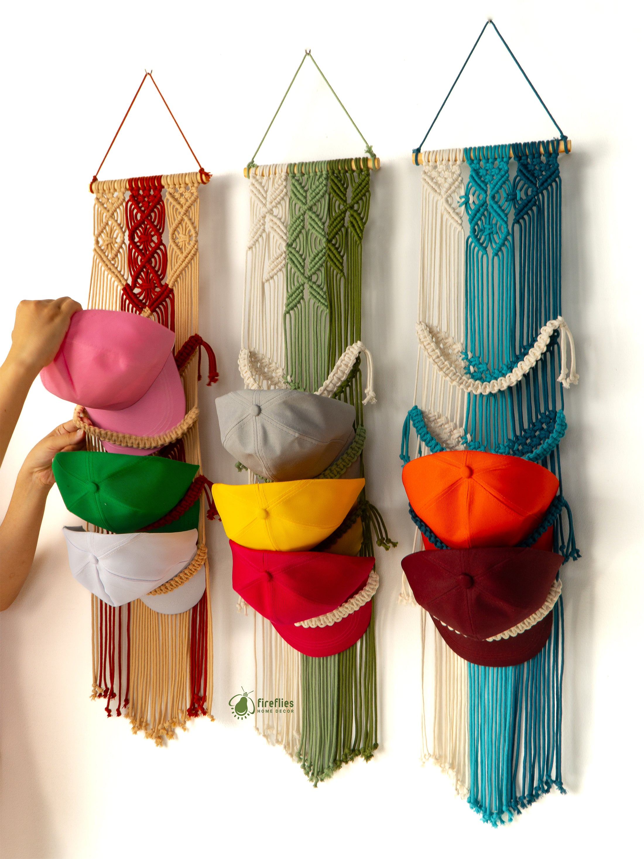 Colorful macrame hat rack with various hats hanging on it against a white background.