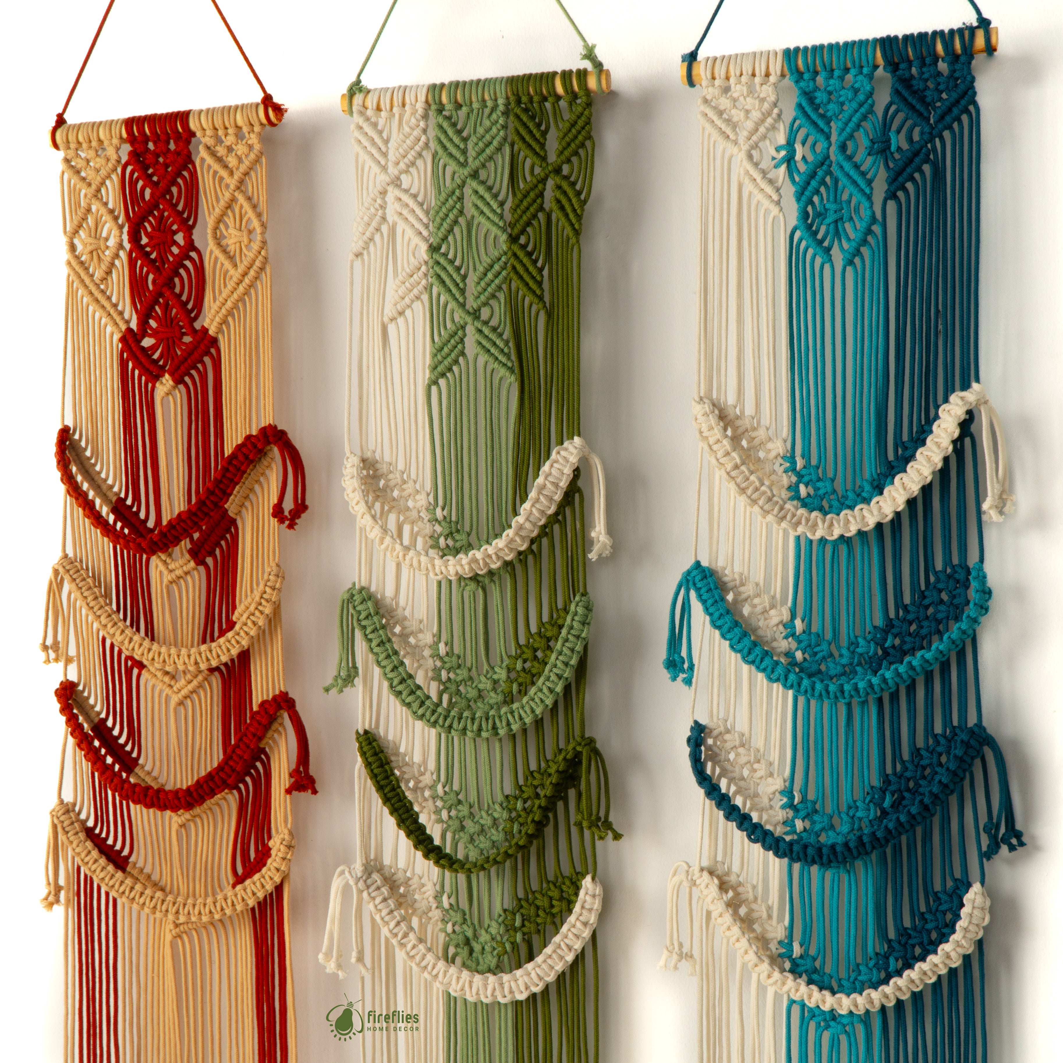 Three macrame wall hangings in red, green, and blue on a white background.