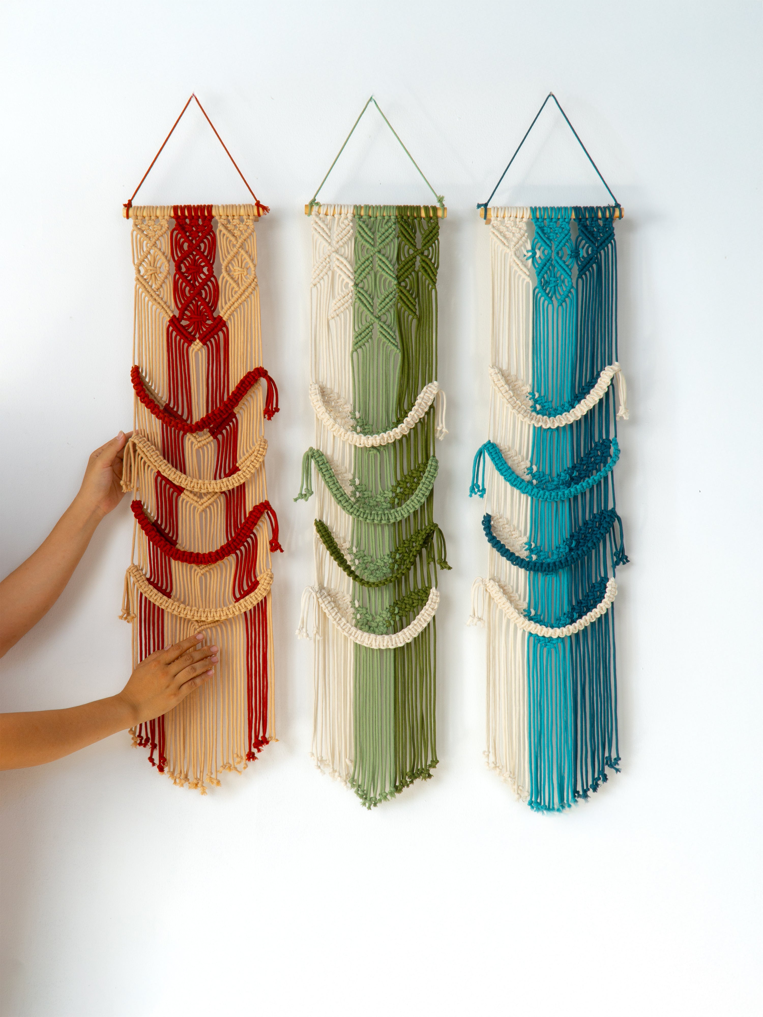 Three colorful wall hangings made from folded fabric with a hand reaching towards one of them.