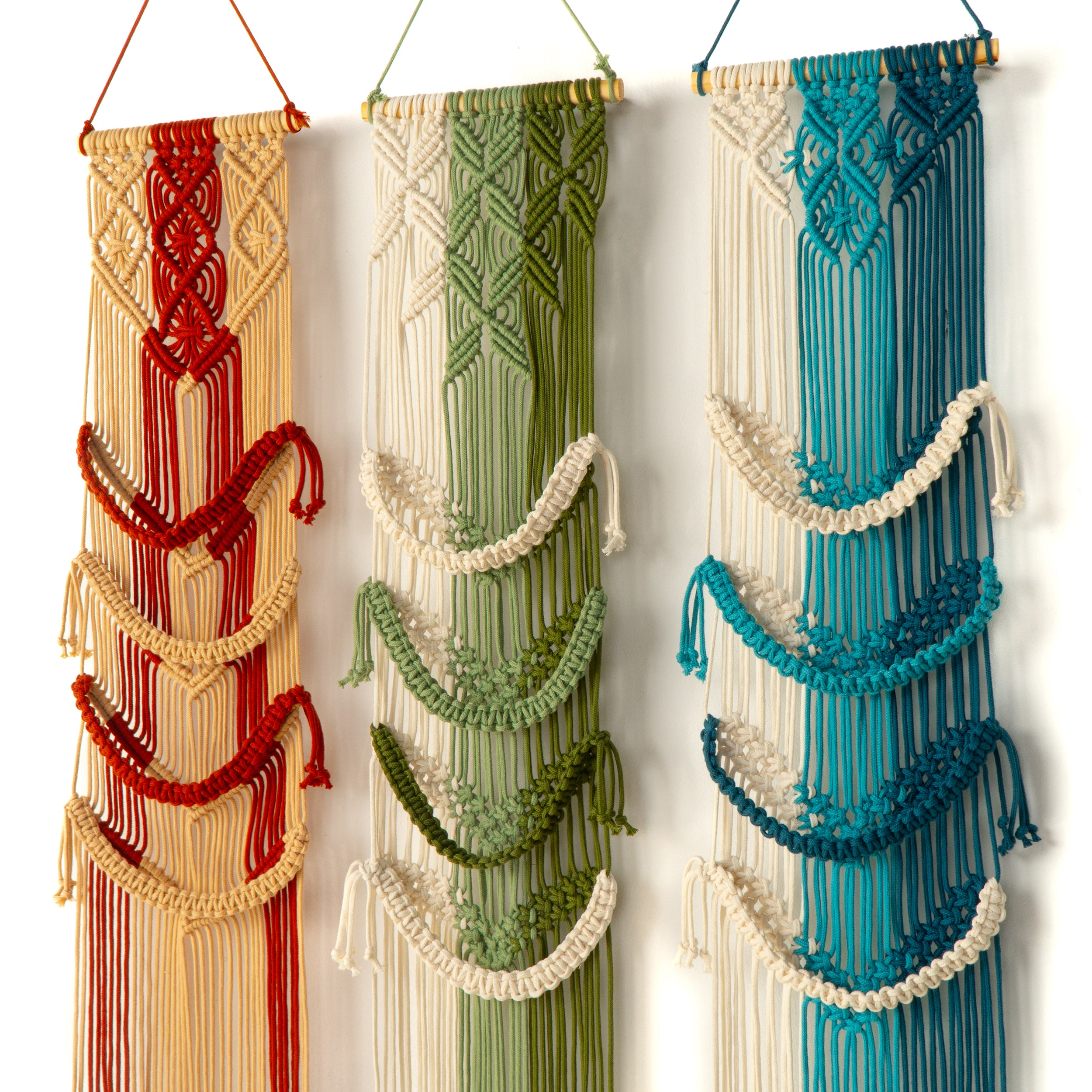 Three colorful macrame wall hangings in red, green, and blue on a white background.