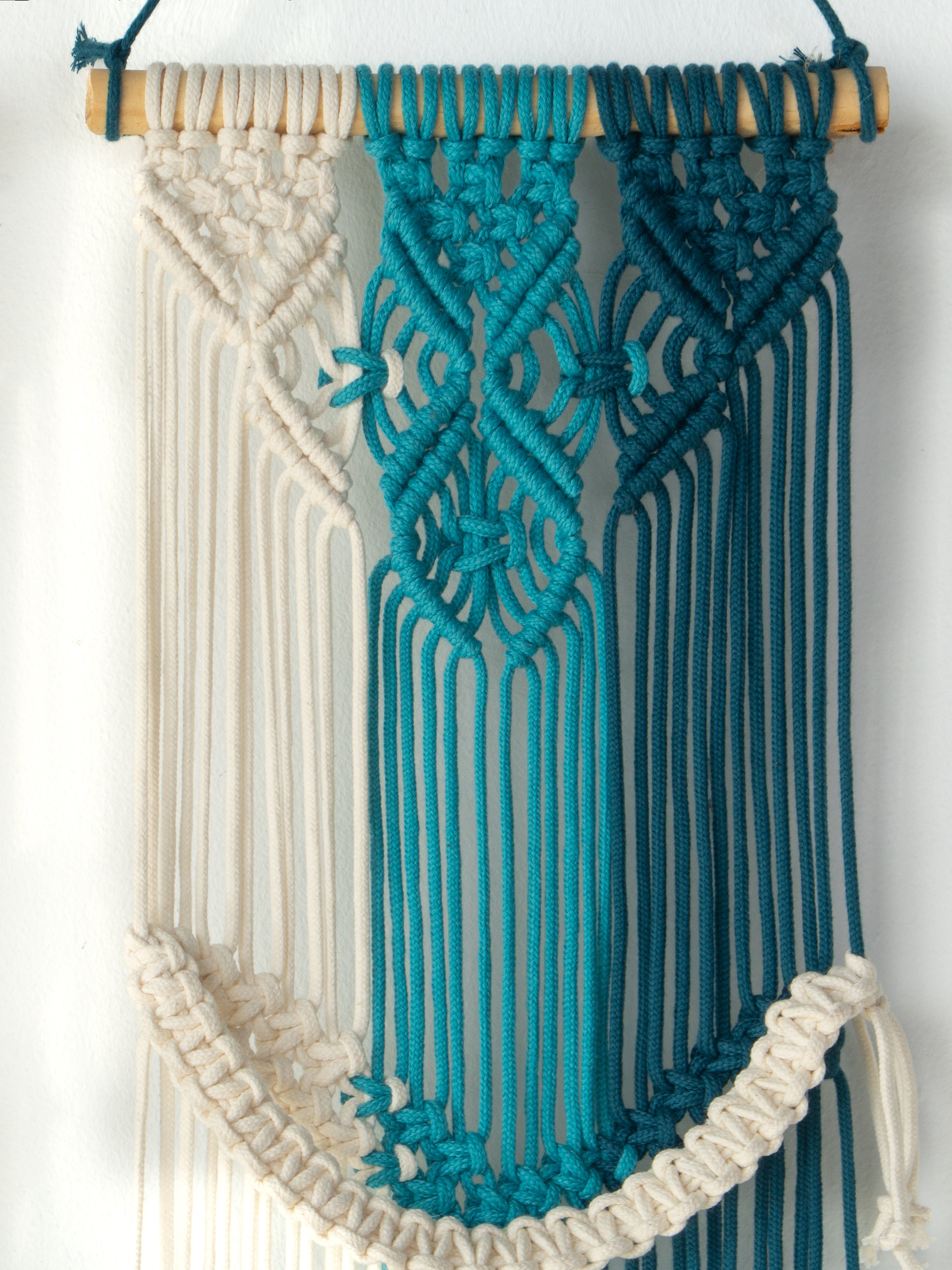 Macrame wall hanging with blue and white strings on a wooden frame.