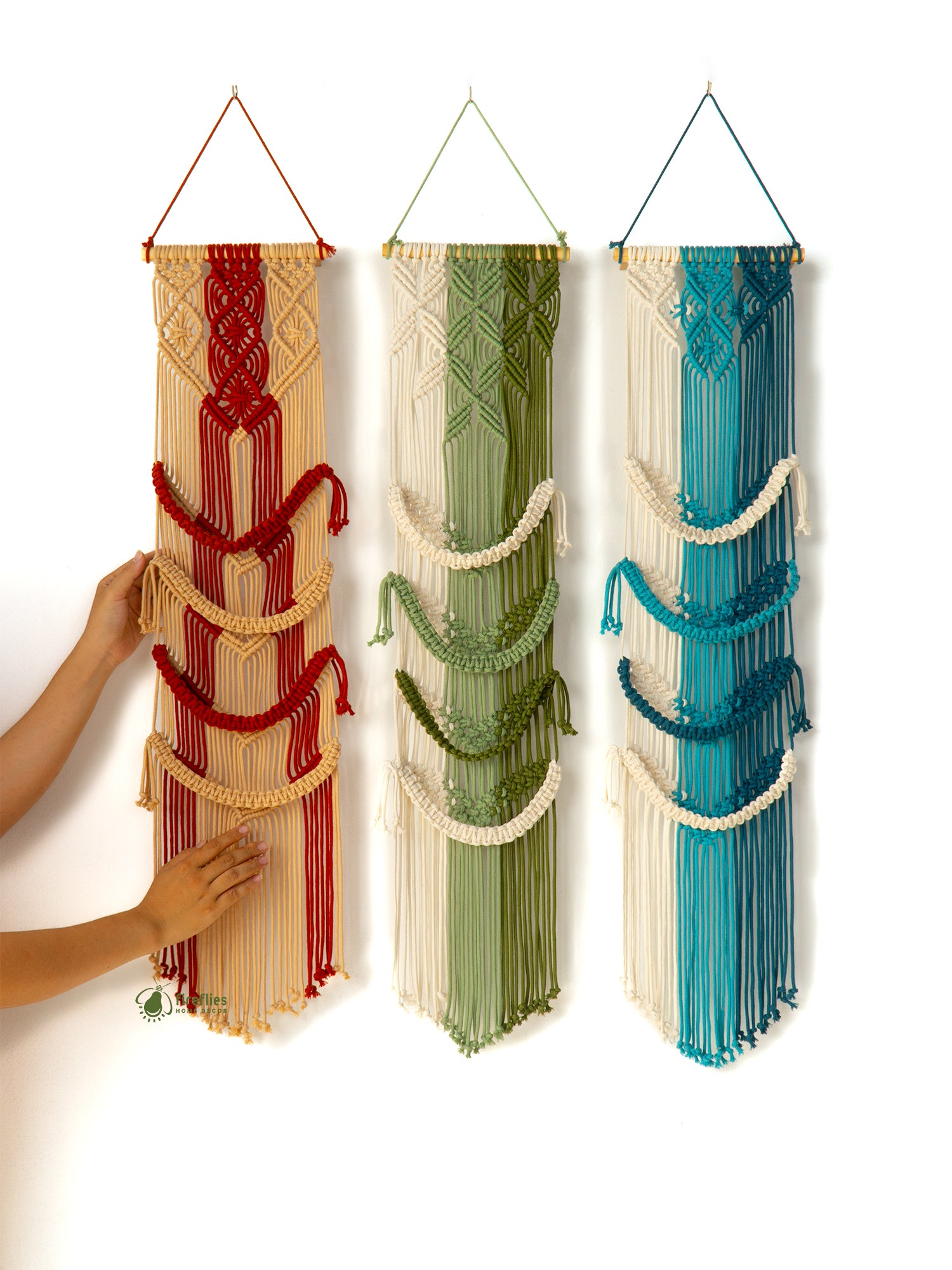 Three colorful macrame wall hangings in red, green, and blue on a white background.