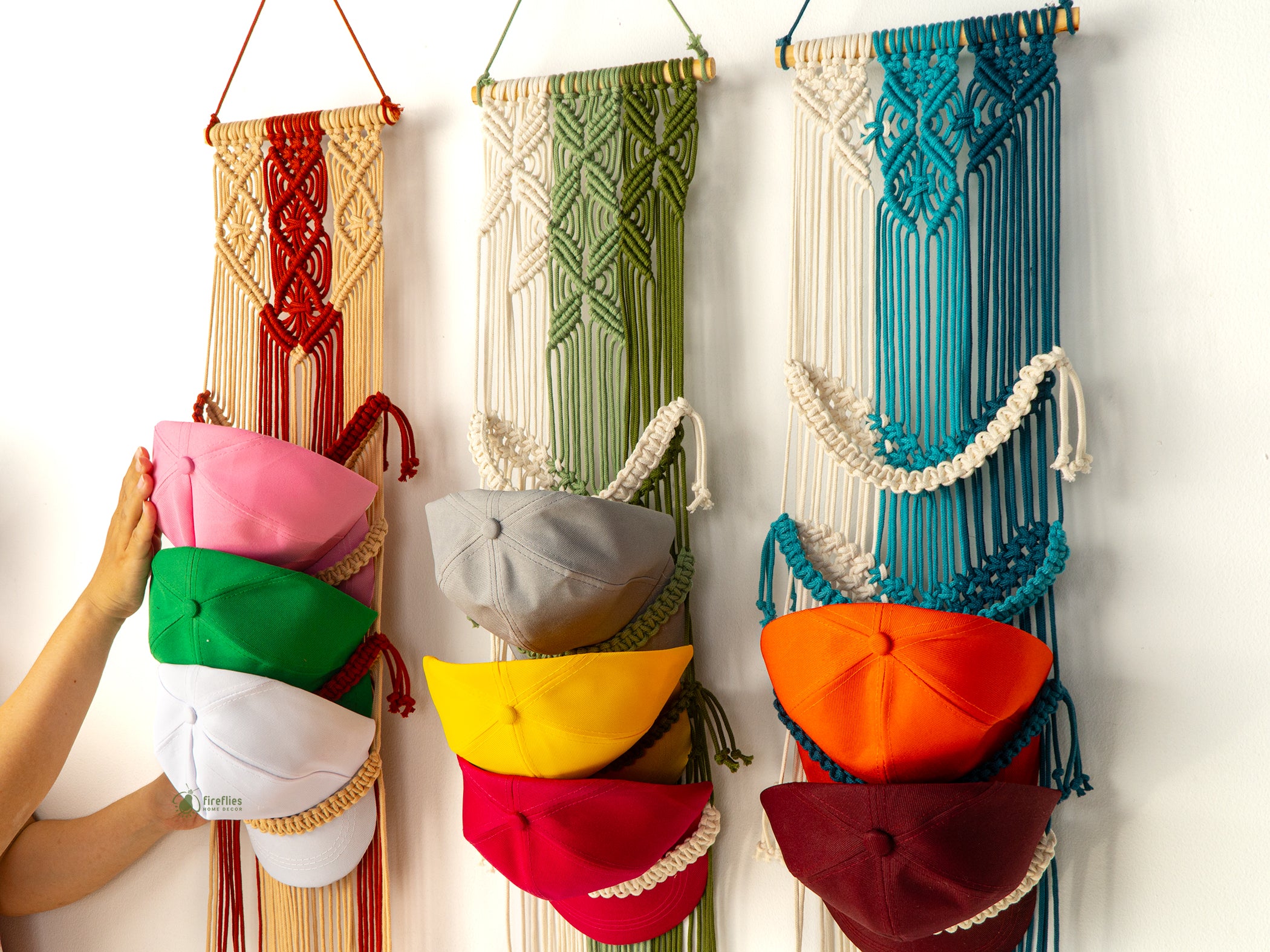 Colorful hats hanging on a macrame wall hanging against a white background