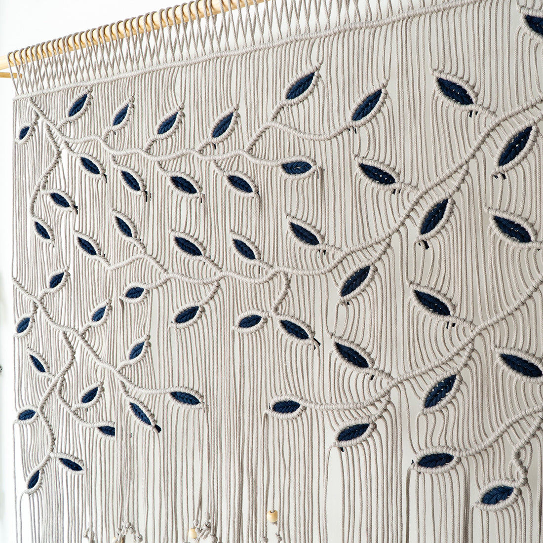 Wide horizontal fiber art in greige macrame cord featuring high-contrast navy blue leaf highlights.