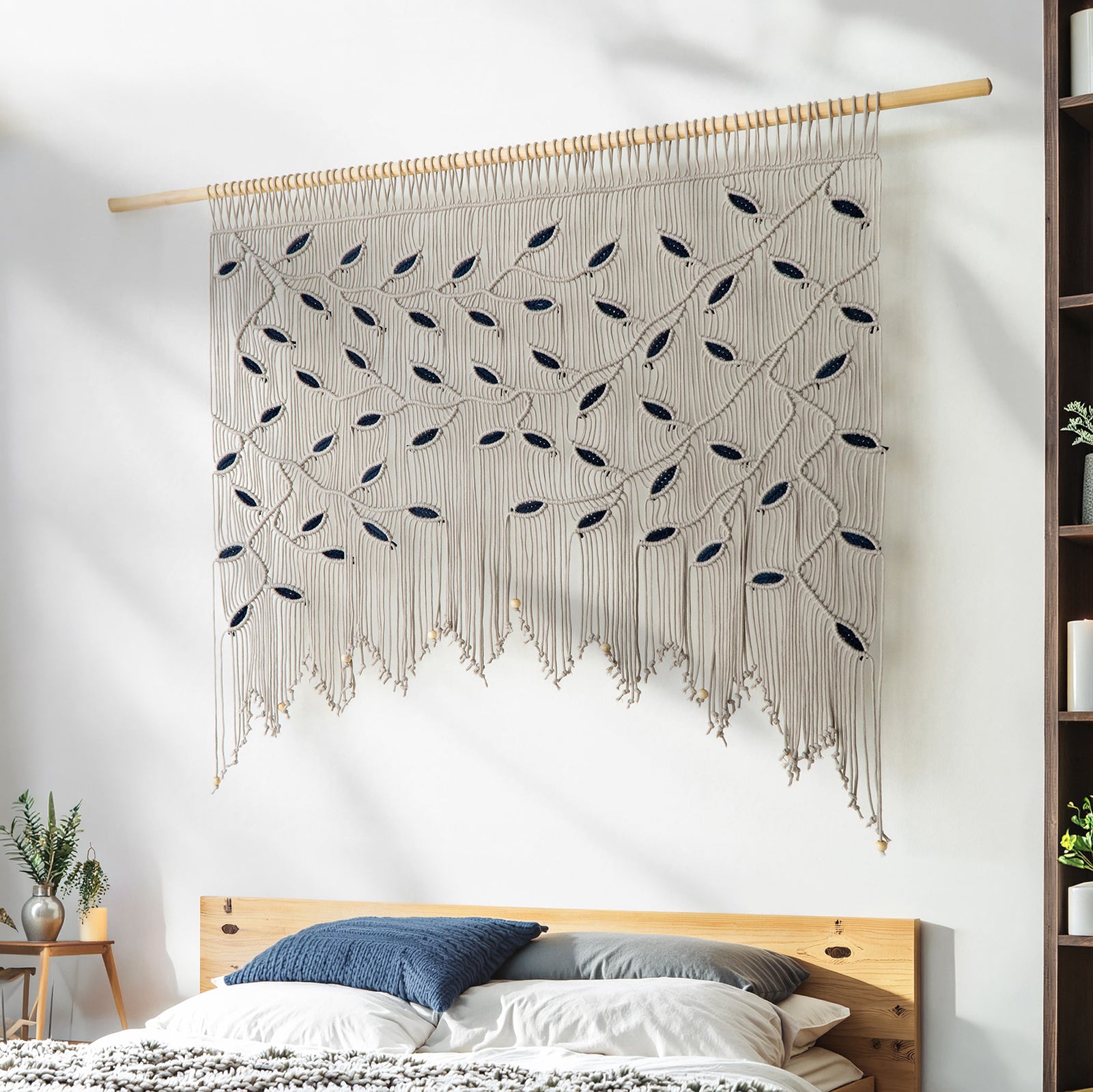 Macrame wall hanging with leaf patterns above a bed in a bedroom setting.