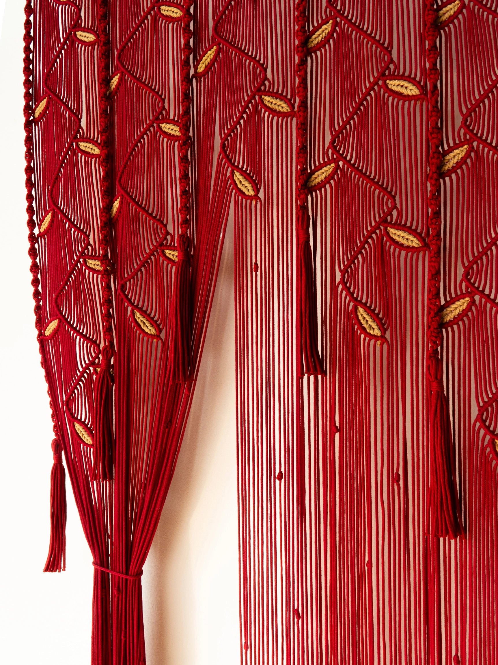 A close-up of a red beaded curtain featuring vertical strands of red beads, leaf-like bead motifs, and tassel ends, shown against a plain light background.