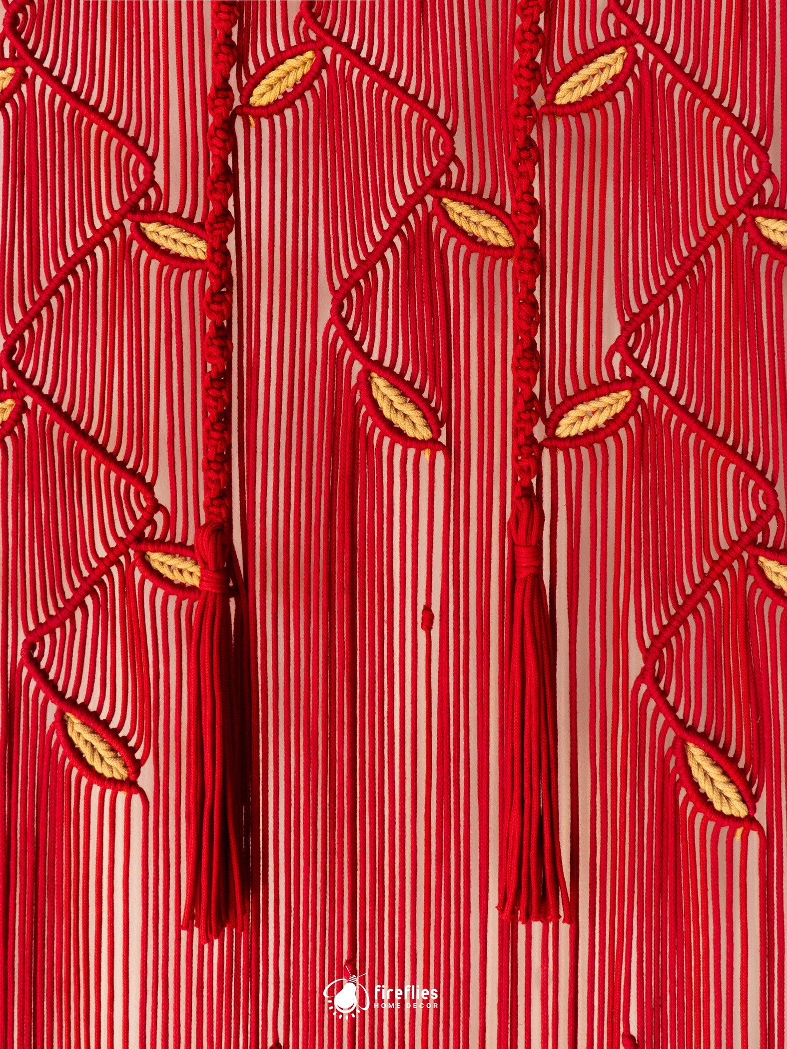 A close-up of a red and white vertically striped fabric with intricate red braided cord patterns, leaf-like woven details, and hanging tassels. A small white logo watermark is visible at the bottom center.