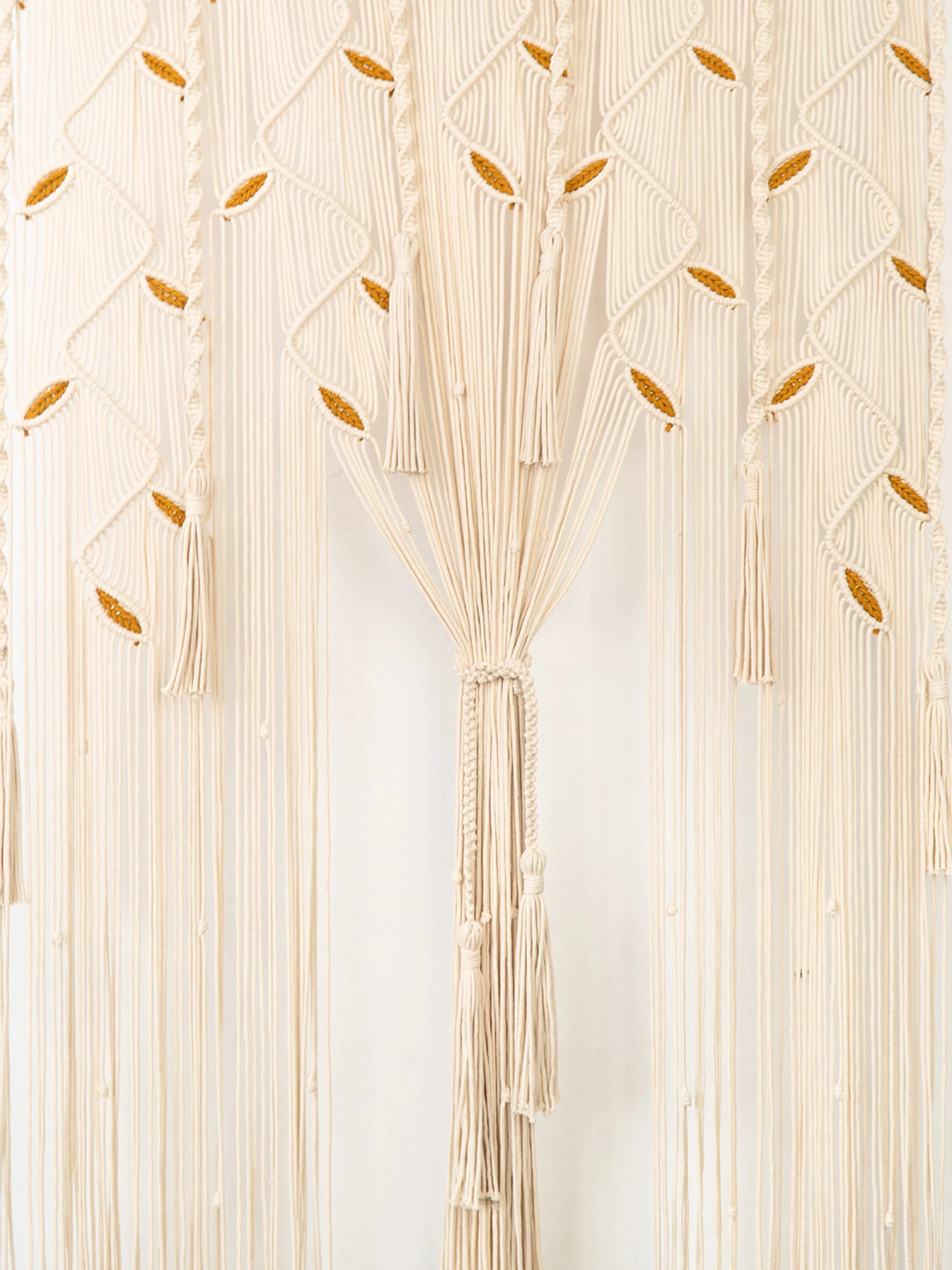 Cream macrame wall hanging with braided tassels and small woven leaf accents, shown against a plain white background.