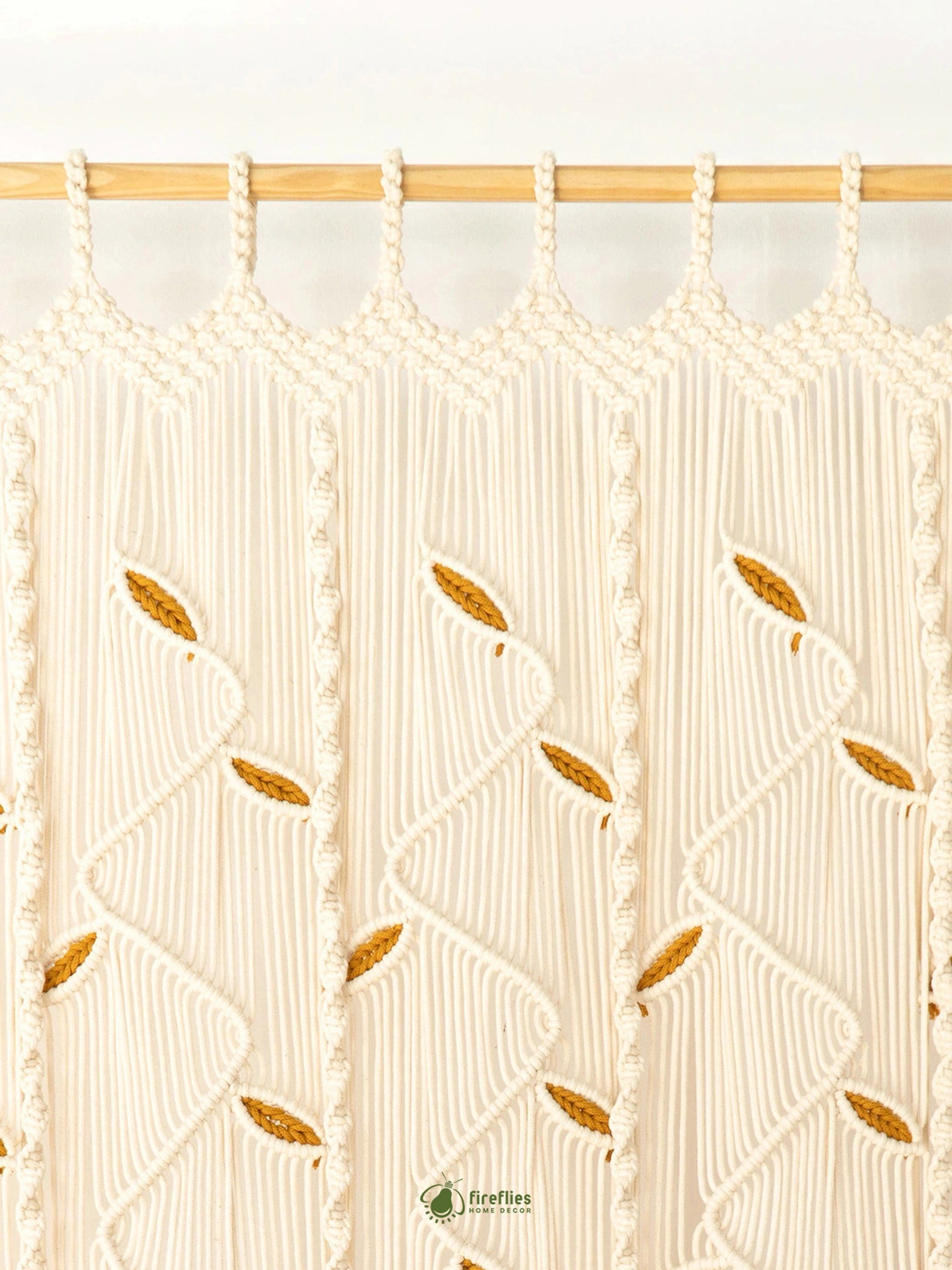 Cream macrame curtain panels hanging from a light wood rod, featuring textured vertical stripes and embroidered leaf motifs.