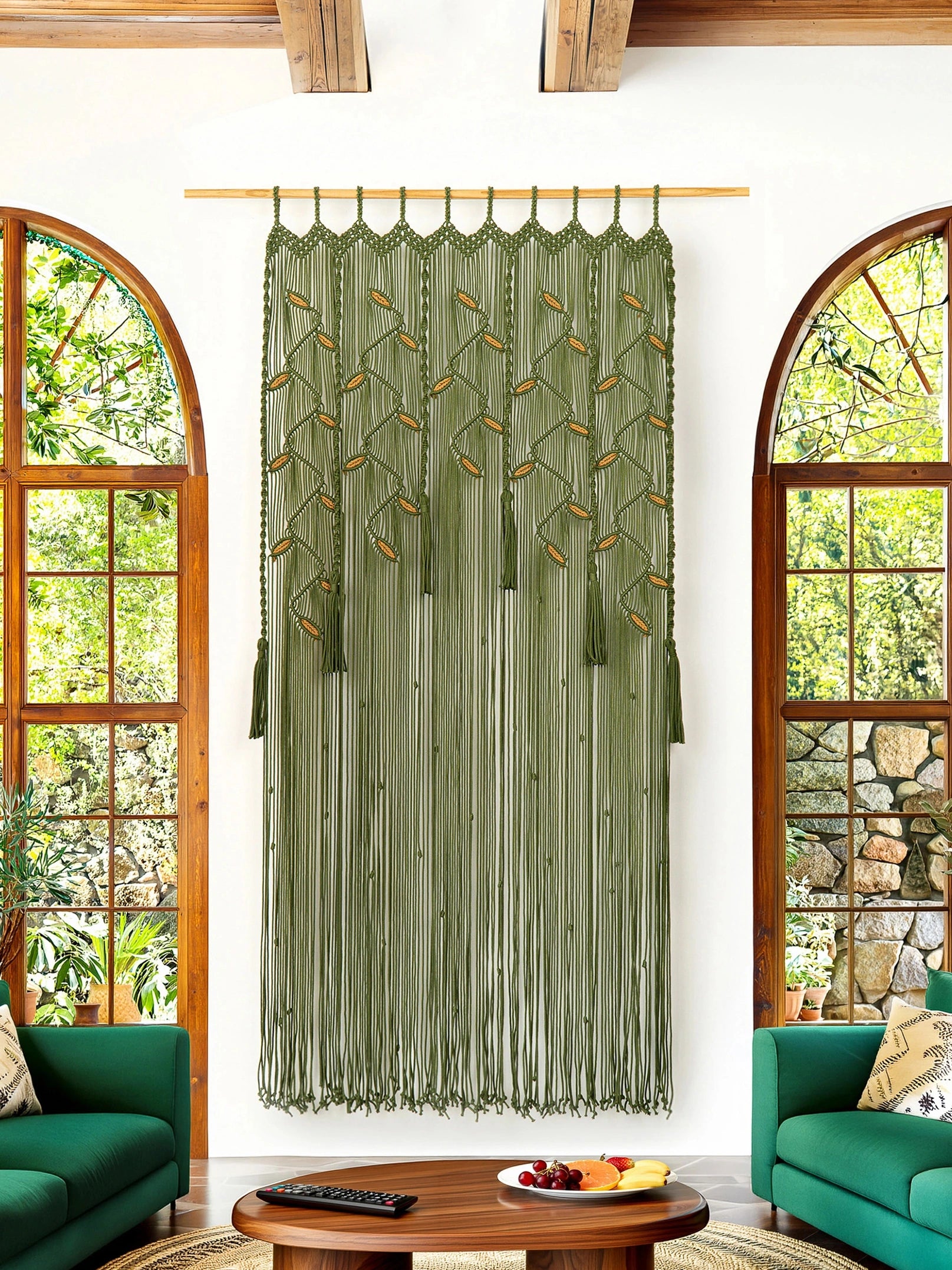 An olive green sheer curtain panel with a geometric trellis pattern and tassel fringe, hanging on a wooden rod in a bright living room with arched windows and green sofas.