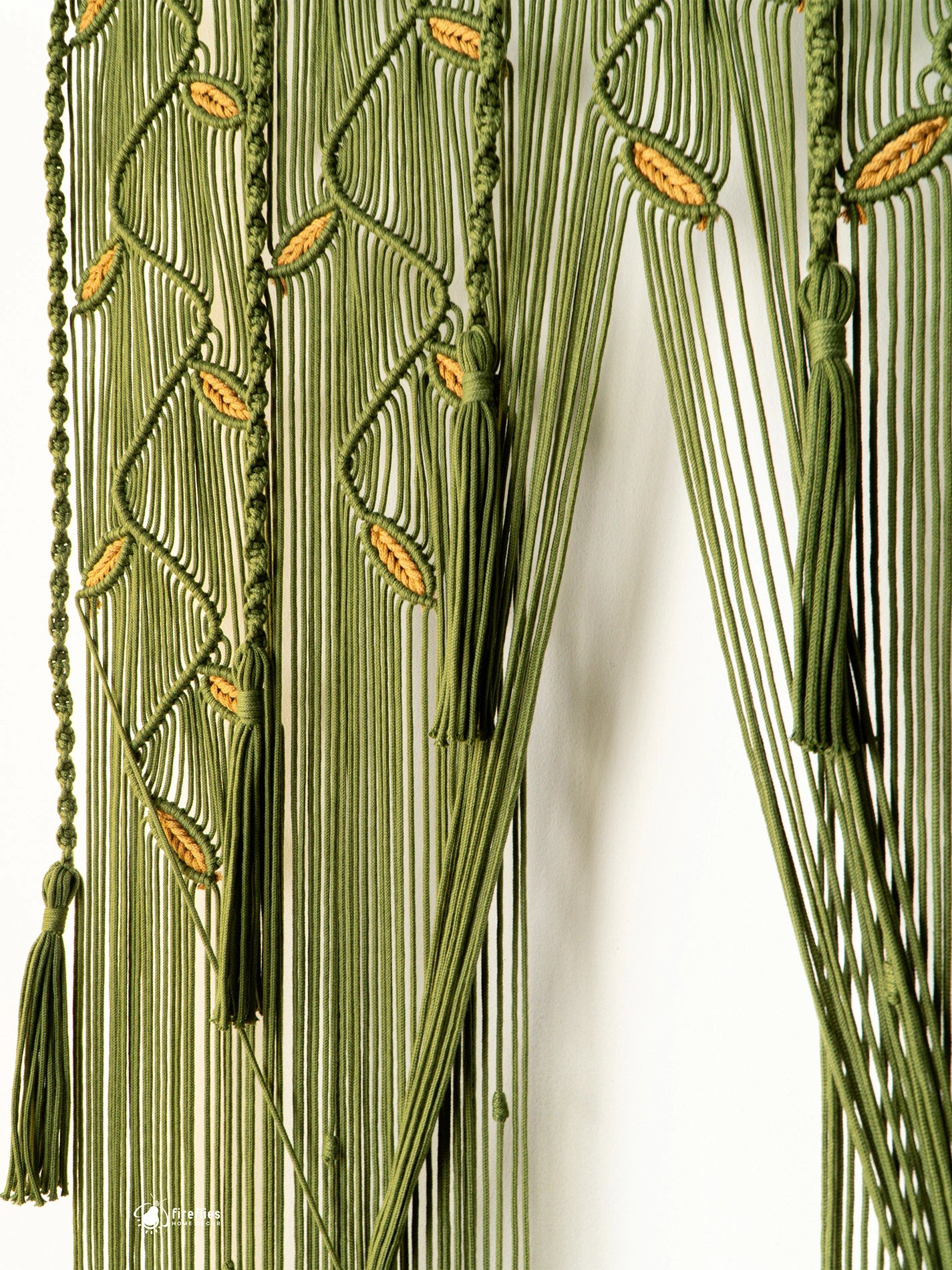 Green fringed curtain with woven leaf patterns and tassels, shown hanging against a white background.