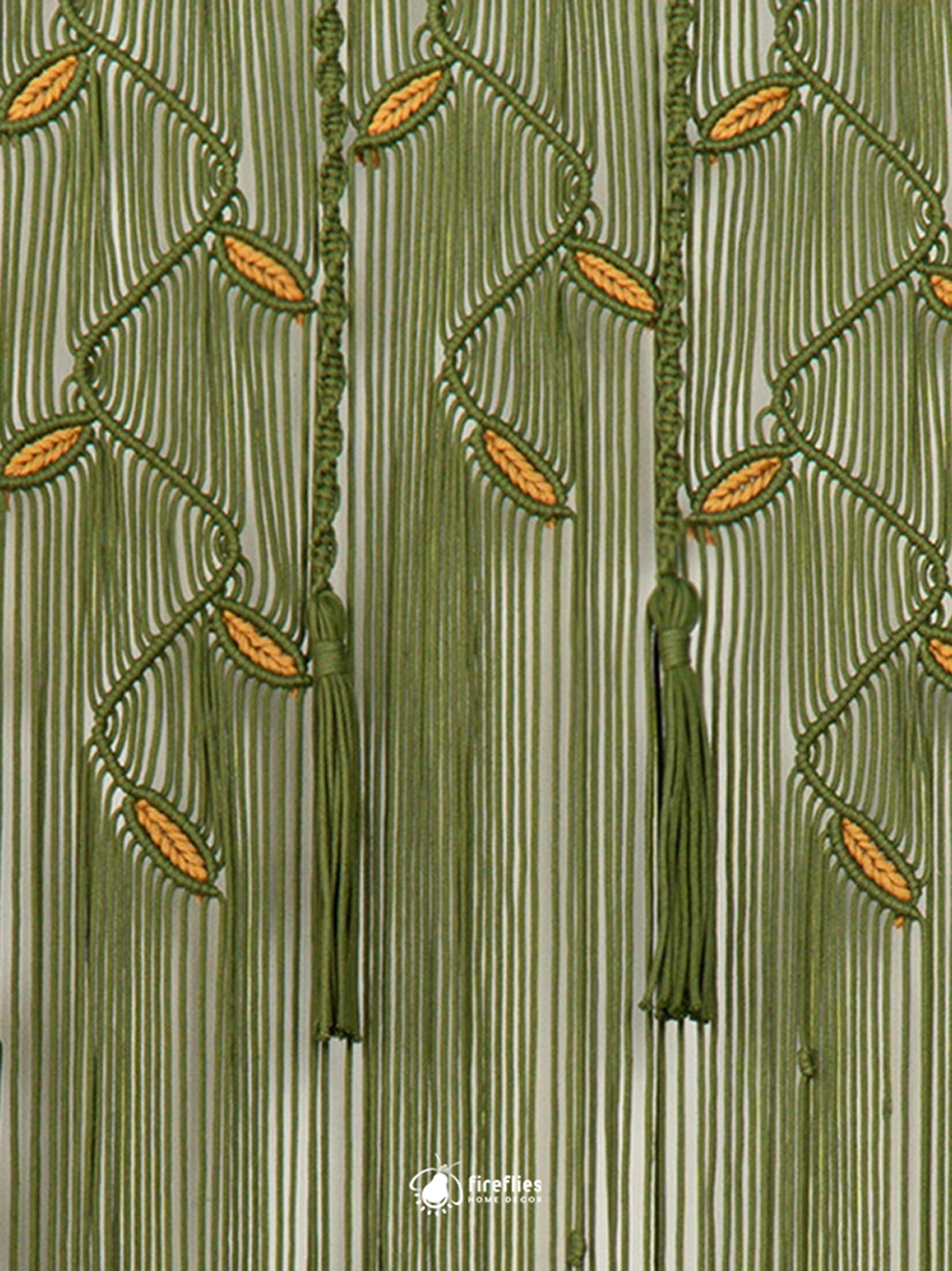A close-up of a green beaded curtain featuring vertical hanging cords, leaf-like bead clusters, and tassels on a striped fabric background. A small logo watermark is visible at the bottom center.