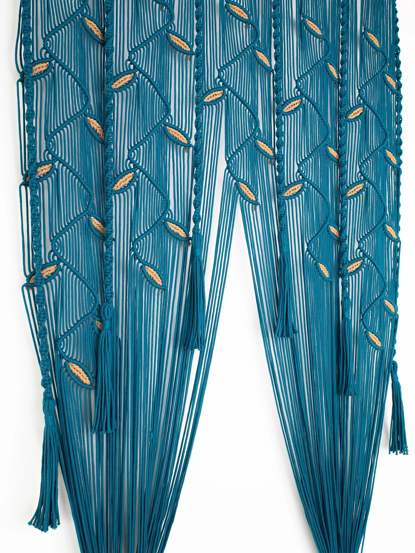 A teal blue macrame curtain featuring geometric woven patterns and hanging tassels, shown against a plain white background.