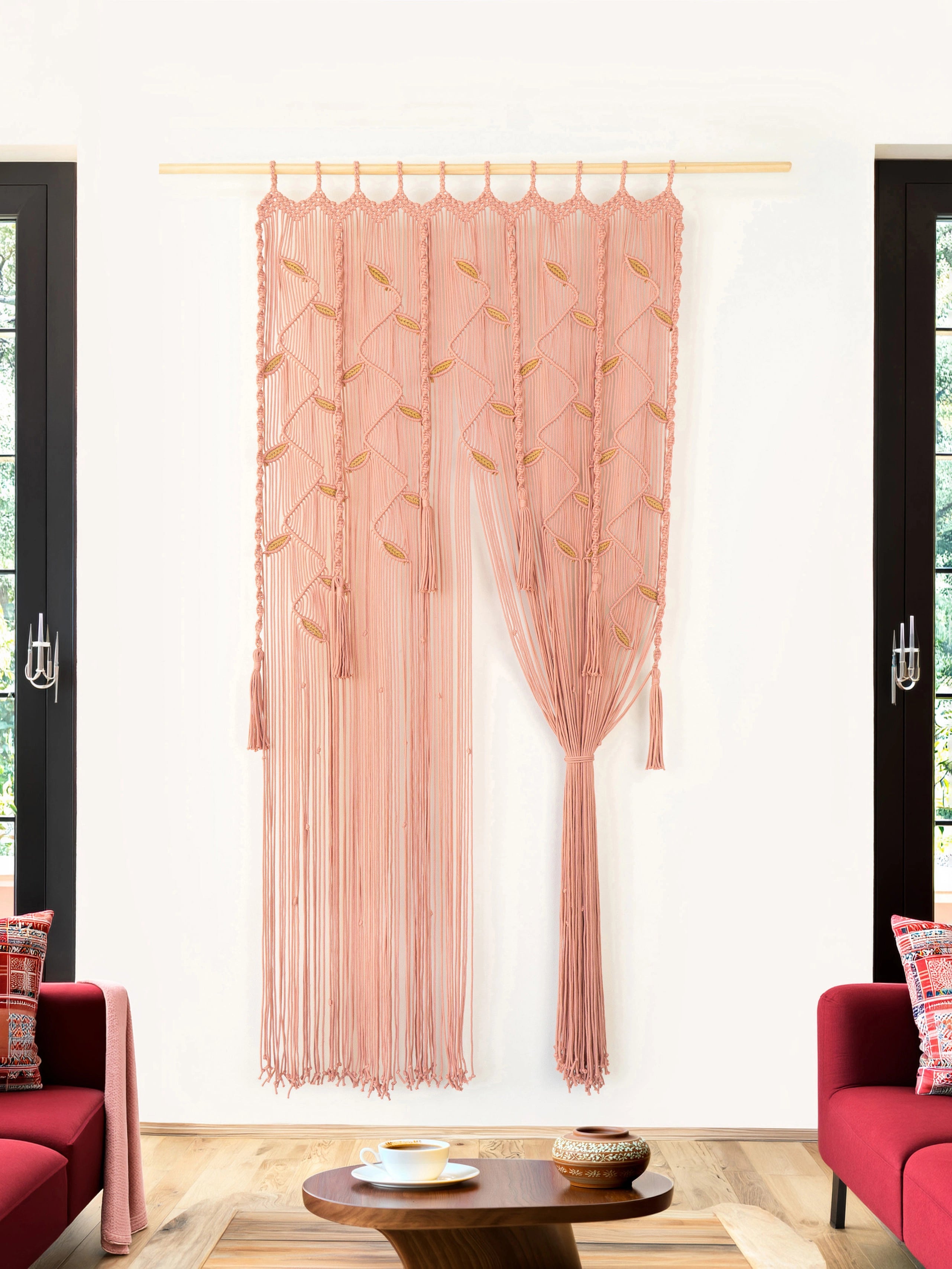 A dusty pink sheer curtain panel with gold embroidered leaf patterns hangs from a light wood rod in a modern living room setting with red armchairs and a wooden coffee table.