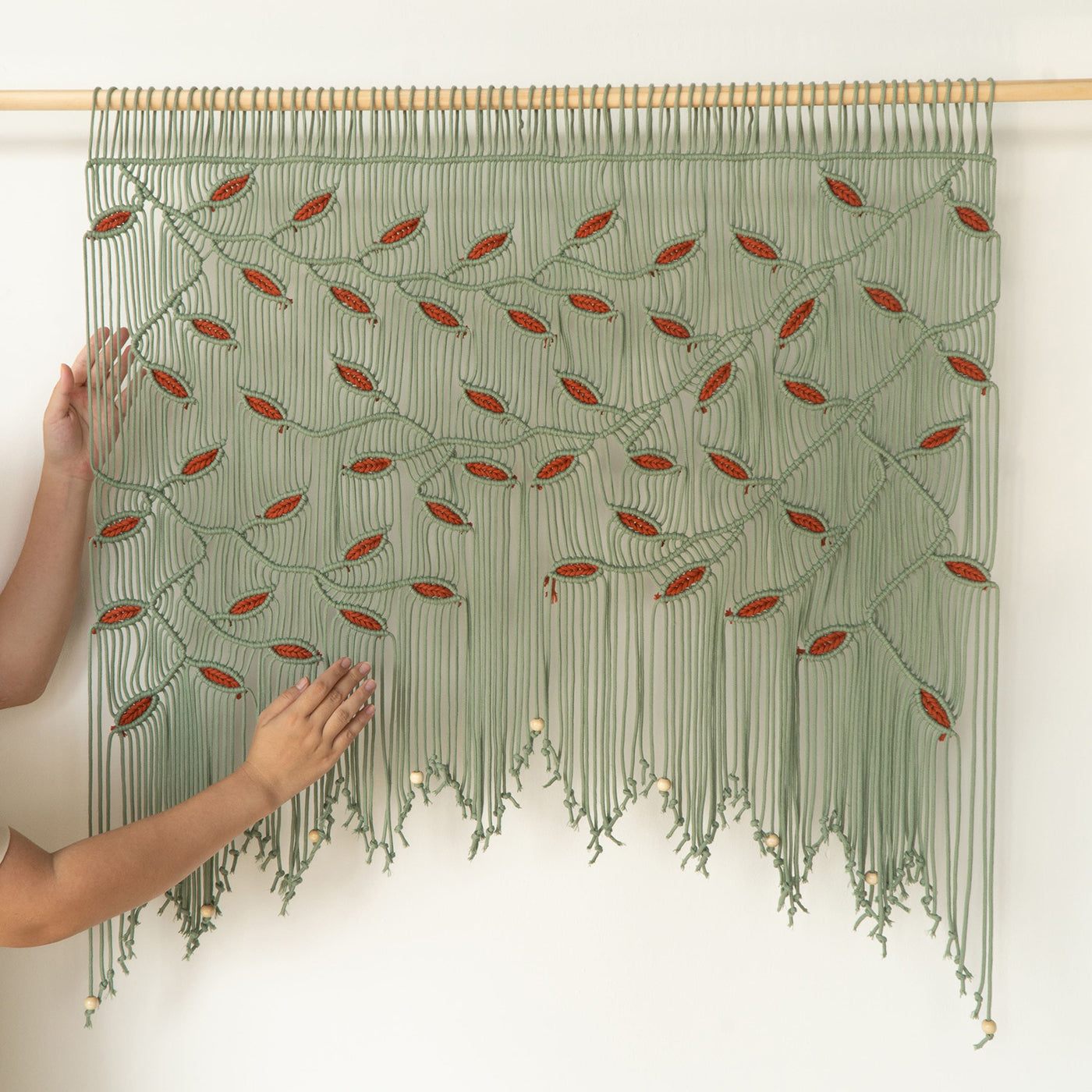 Textile art piece with green and red pattern held by a person against a white background