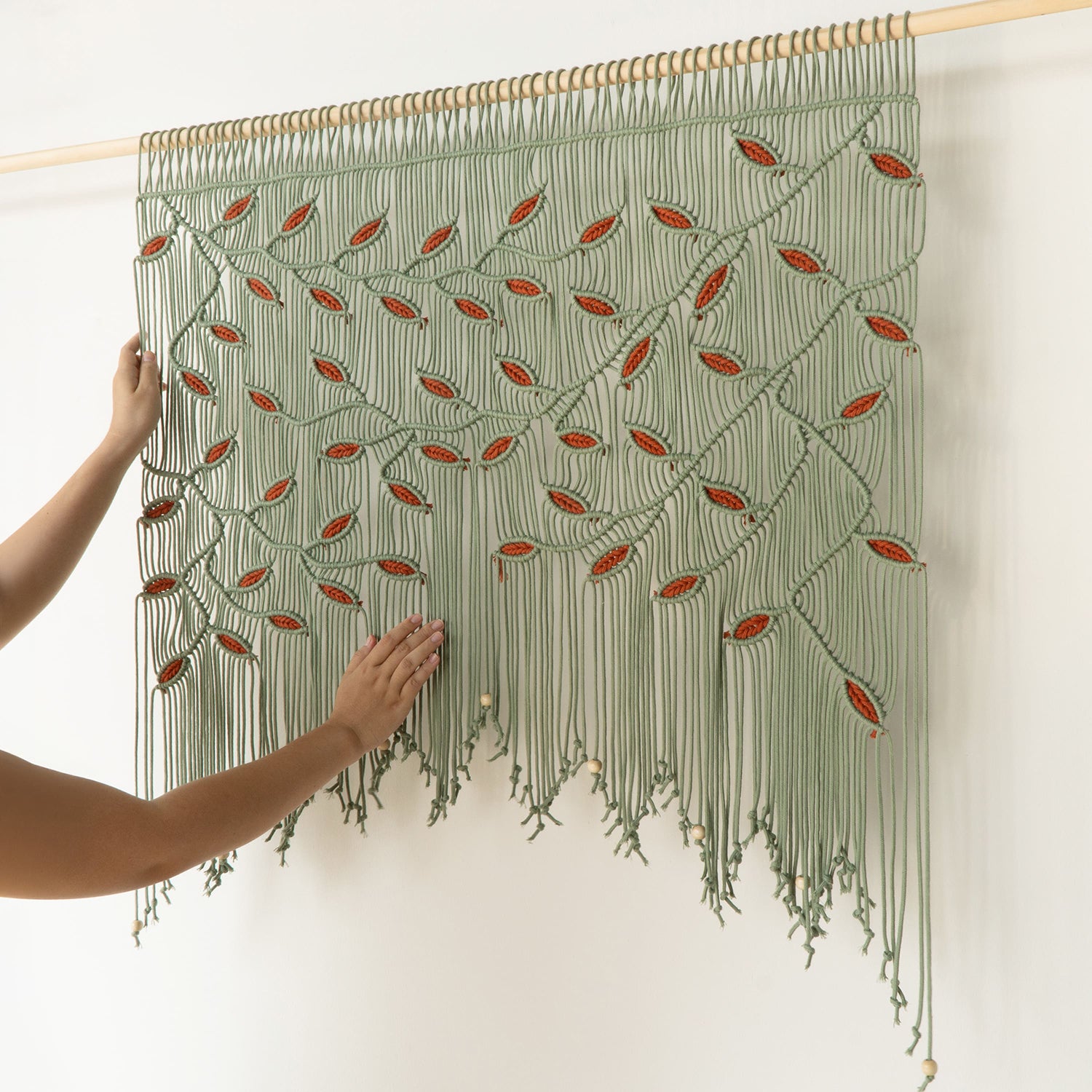 Handmade woven wall art with green and red pattern, held by a person against a white background.