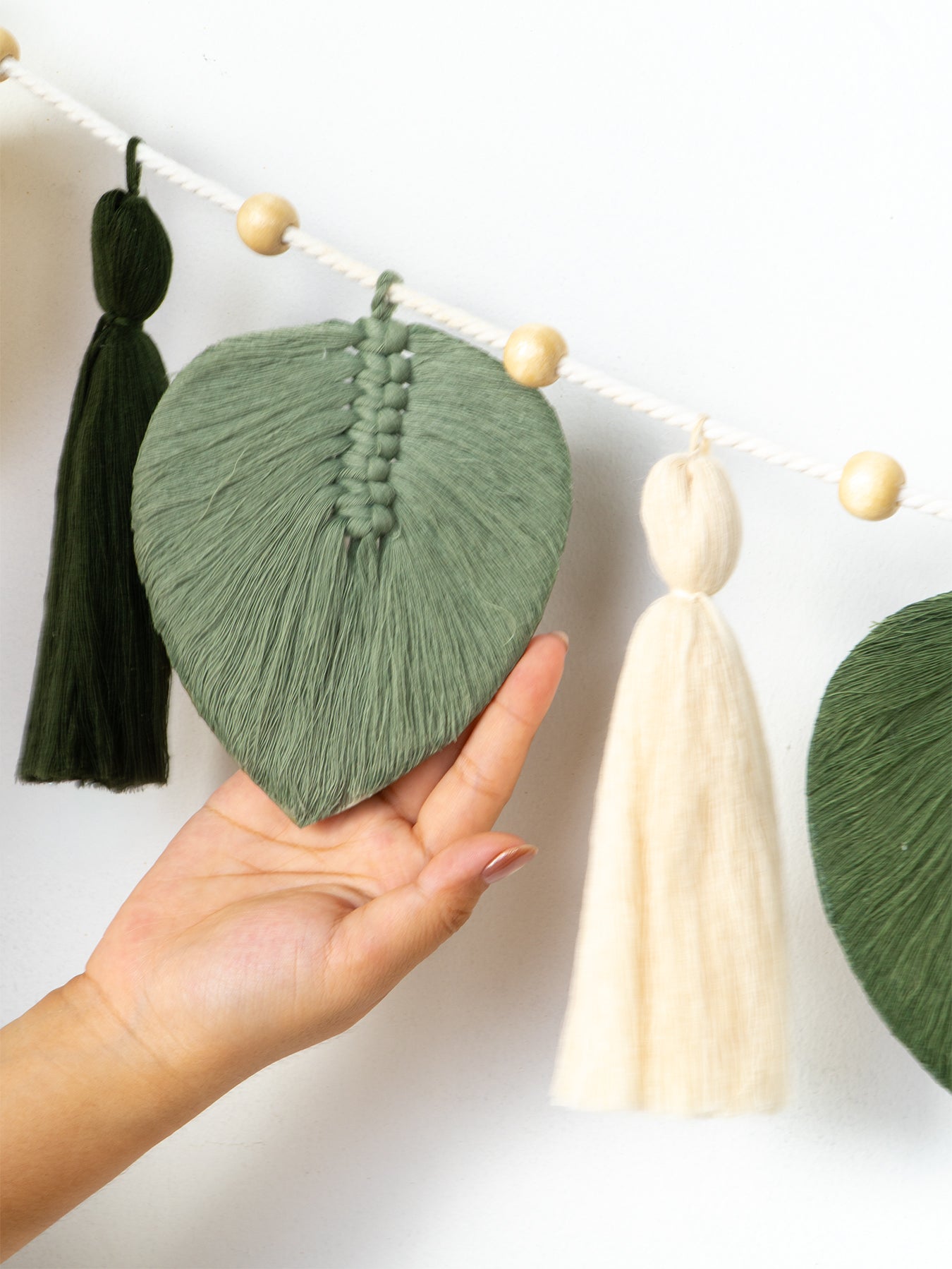 Decorative leaf and tassel wall hanging with a hand holding a green yarn leaf.