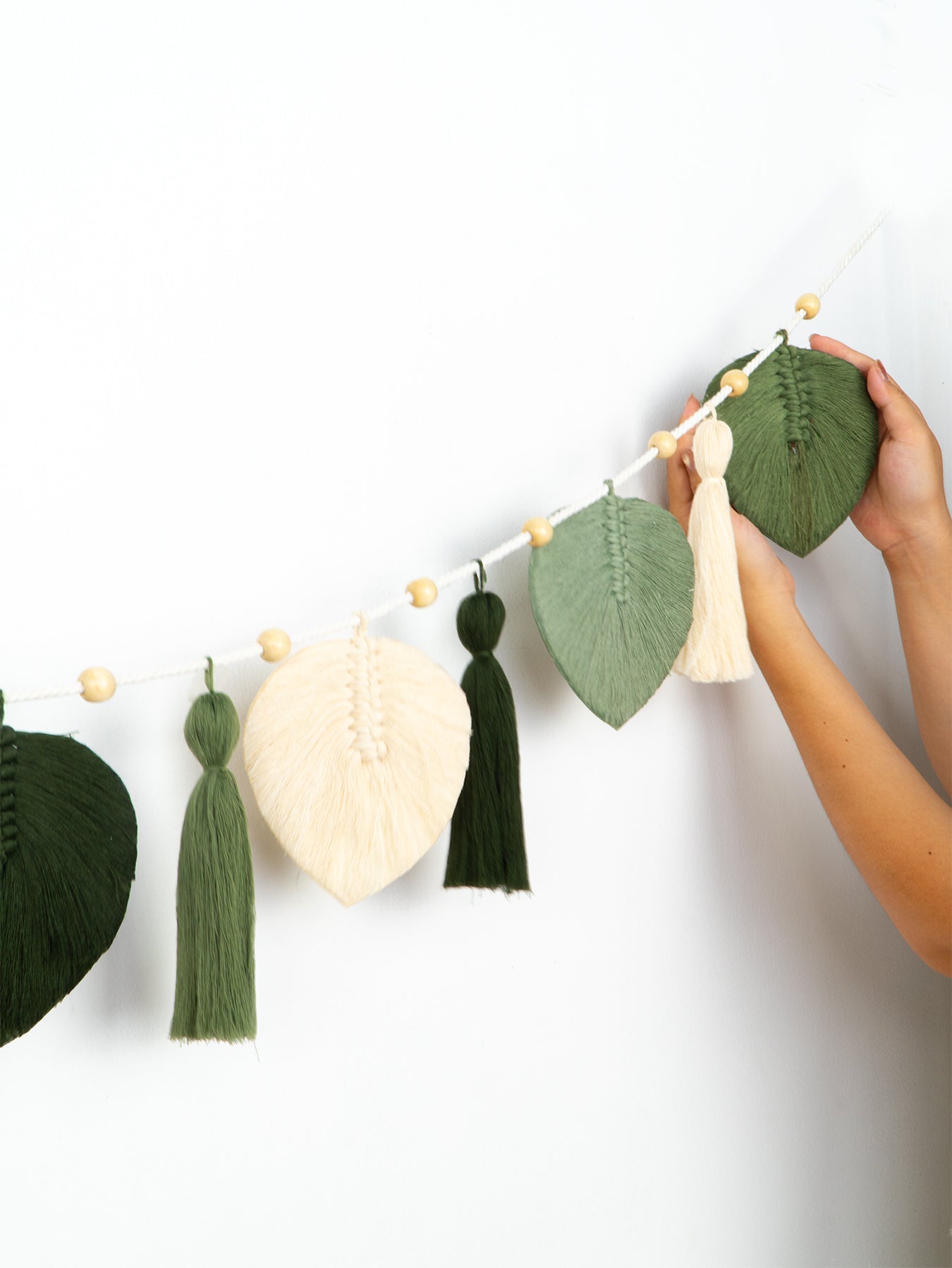 Decorative garland with leaf and tassel elements held by a person against a white background