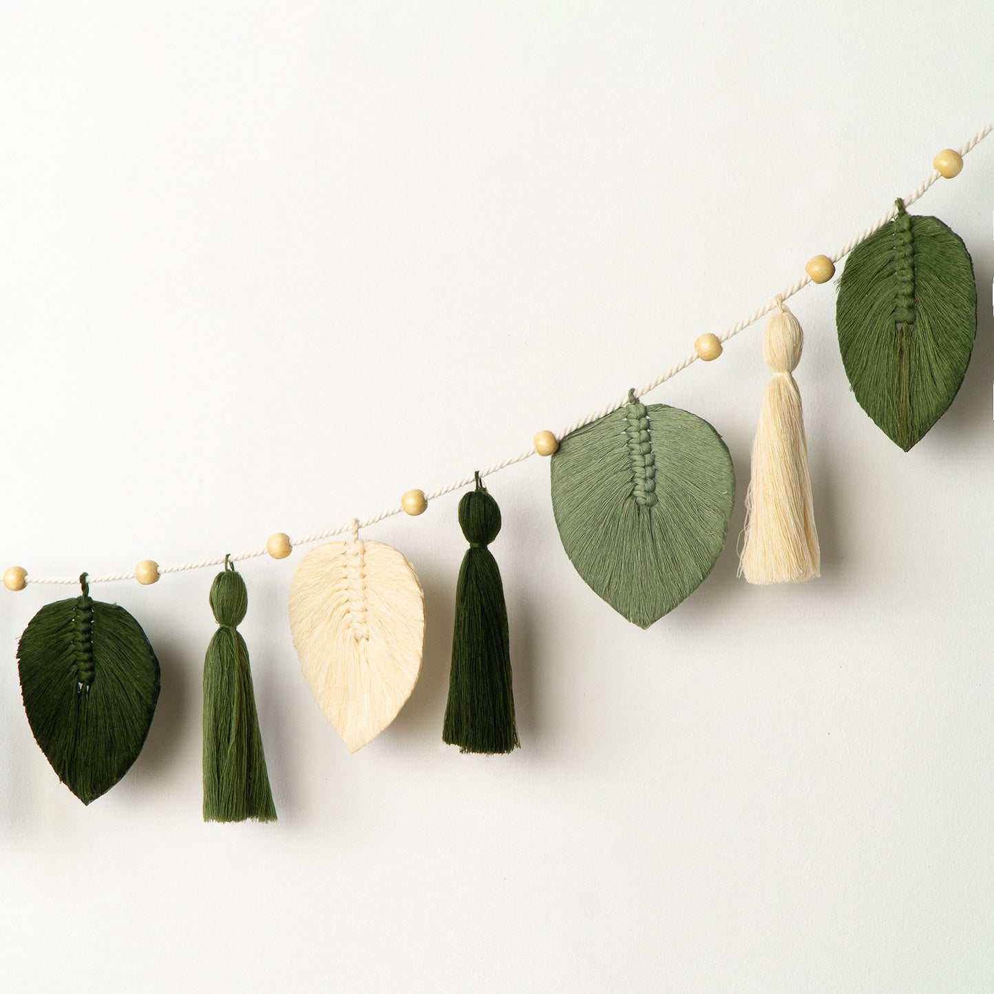 Close-up of a green macrame wall hanging with gold beads on a white background
