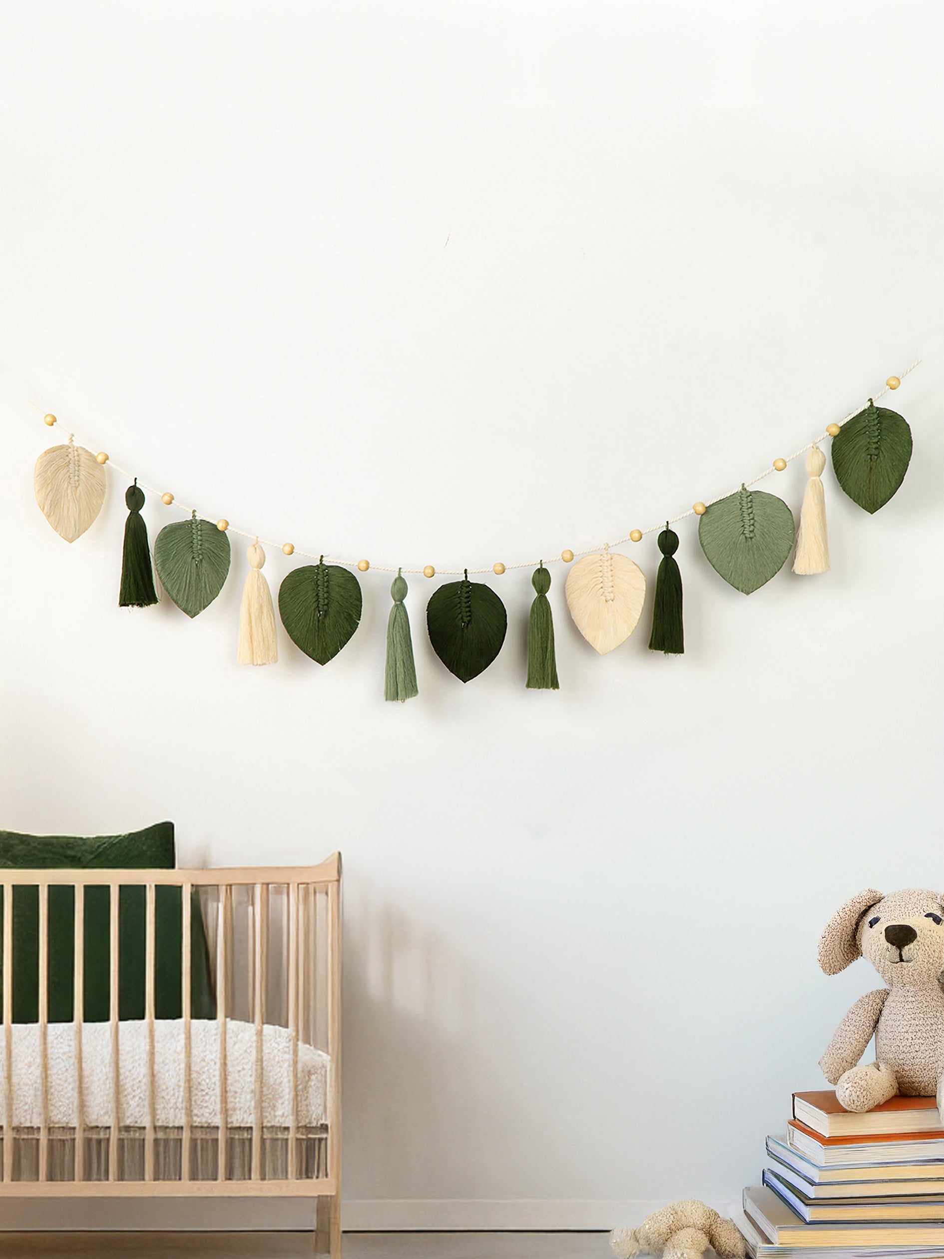Nursery room with crib, decorative leaf garland, and books on a white wall.
