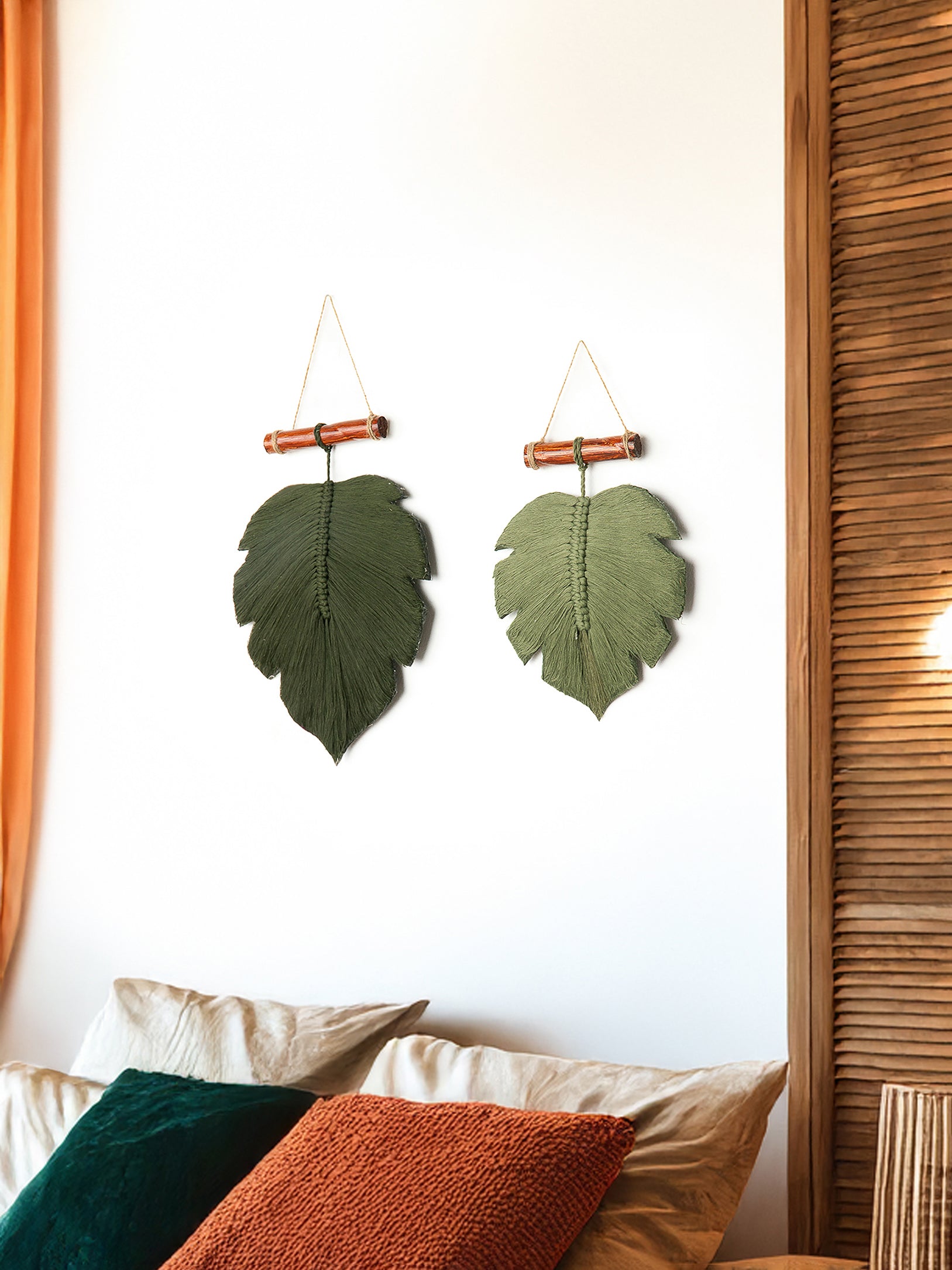 Two leaf-shaped wall hangings on a white wall with pillows and a curtain in the foreground.