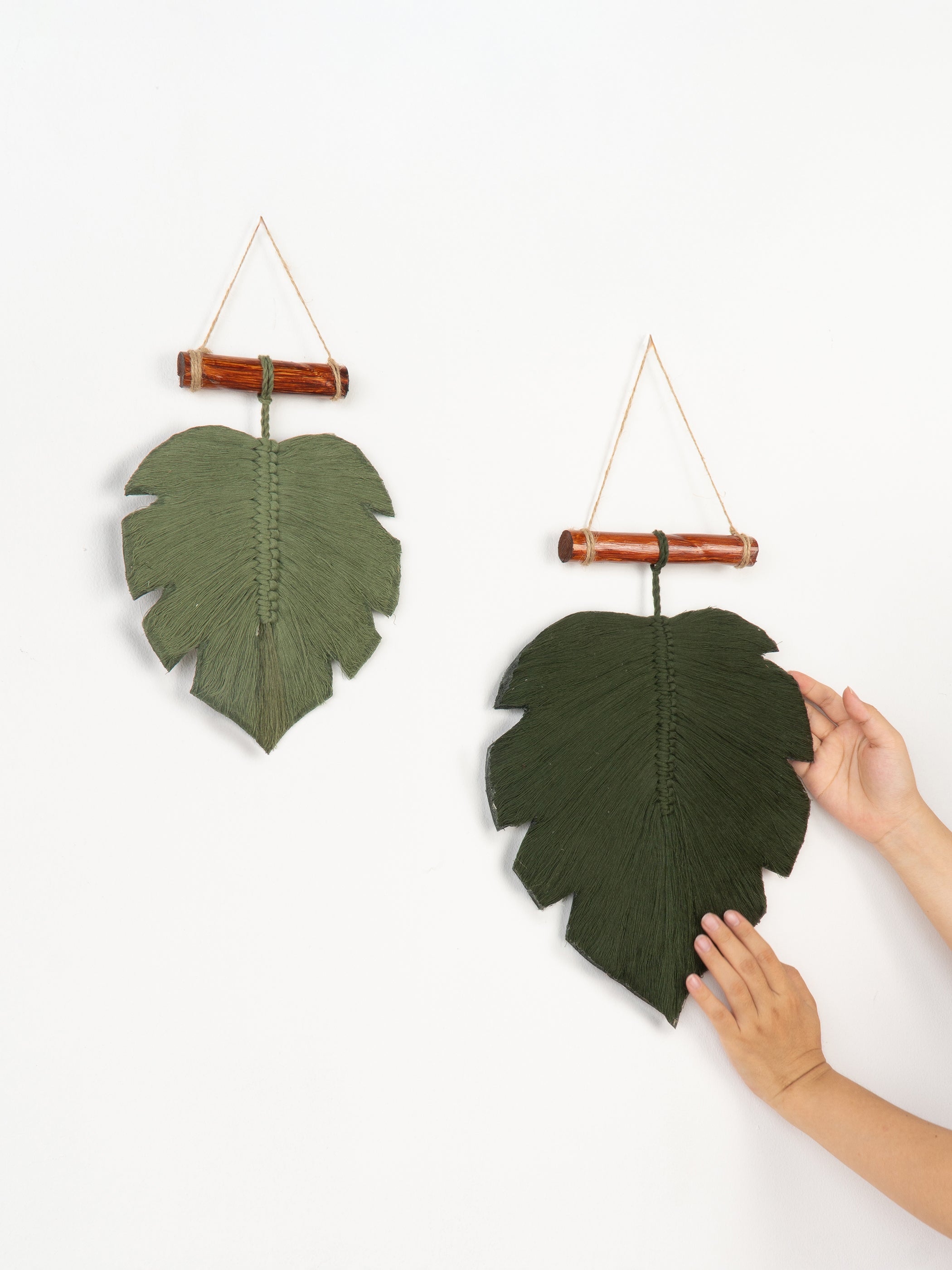 Two green leaf-shaped wall hangings with bamboo sticks on a white background