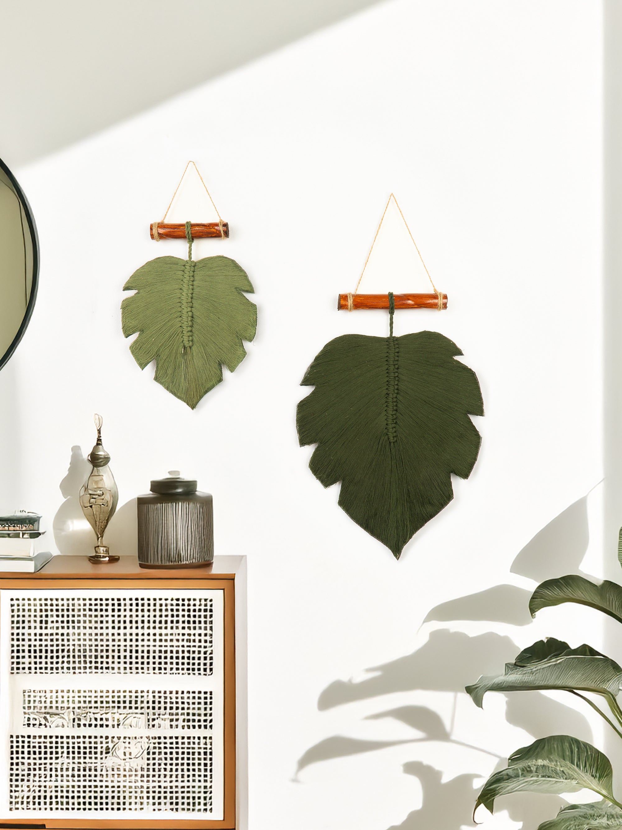 Decorative leaf wall hangings on a white wall with a wooden cabinet and plant in the foreground.