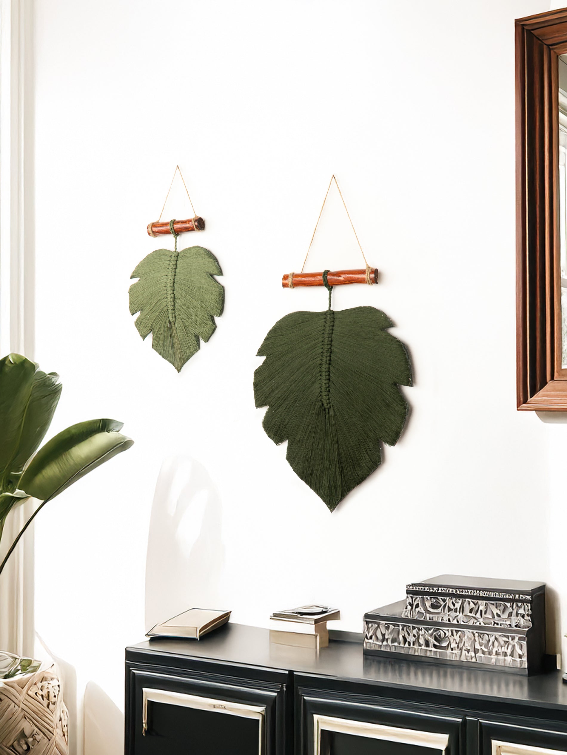 Decorative leaf wall hangings on a white wall with a mirror and books below.