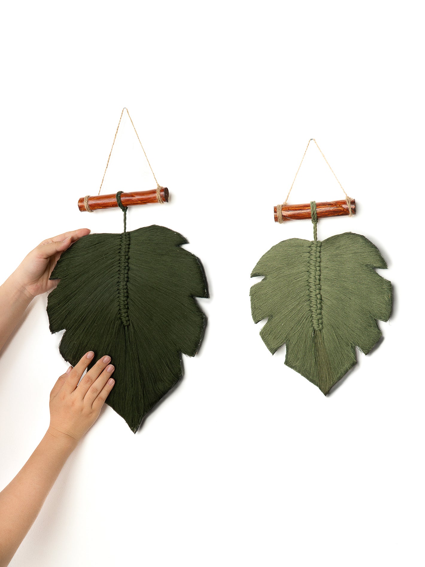 Handmade leaf wall art with a person touching one of the leaves on a white background