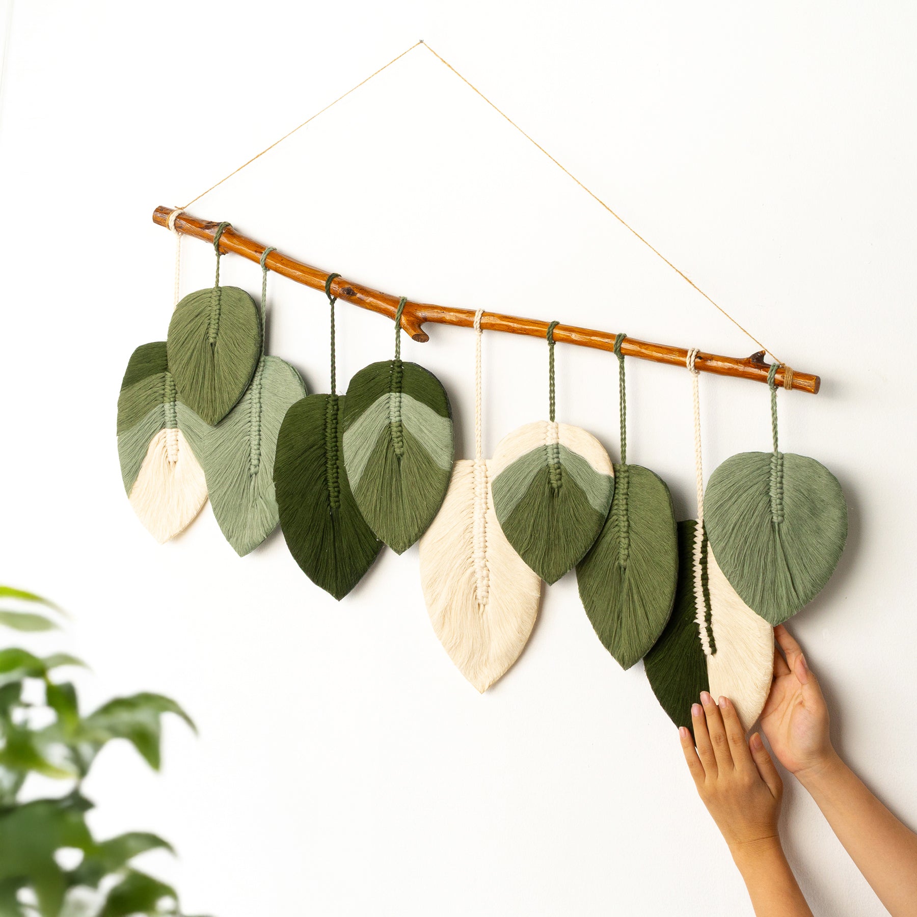 Decorative wall hanging with leaf-shaped fabric pieces on a wooden stick, held by a person's hands.