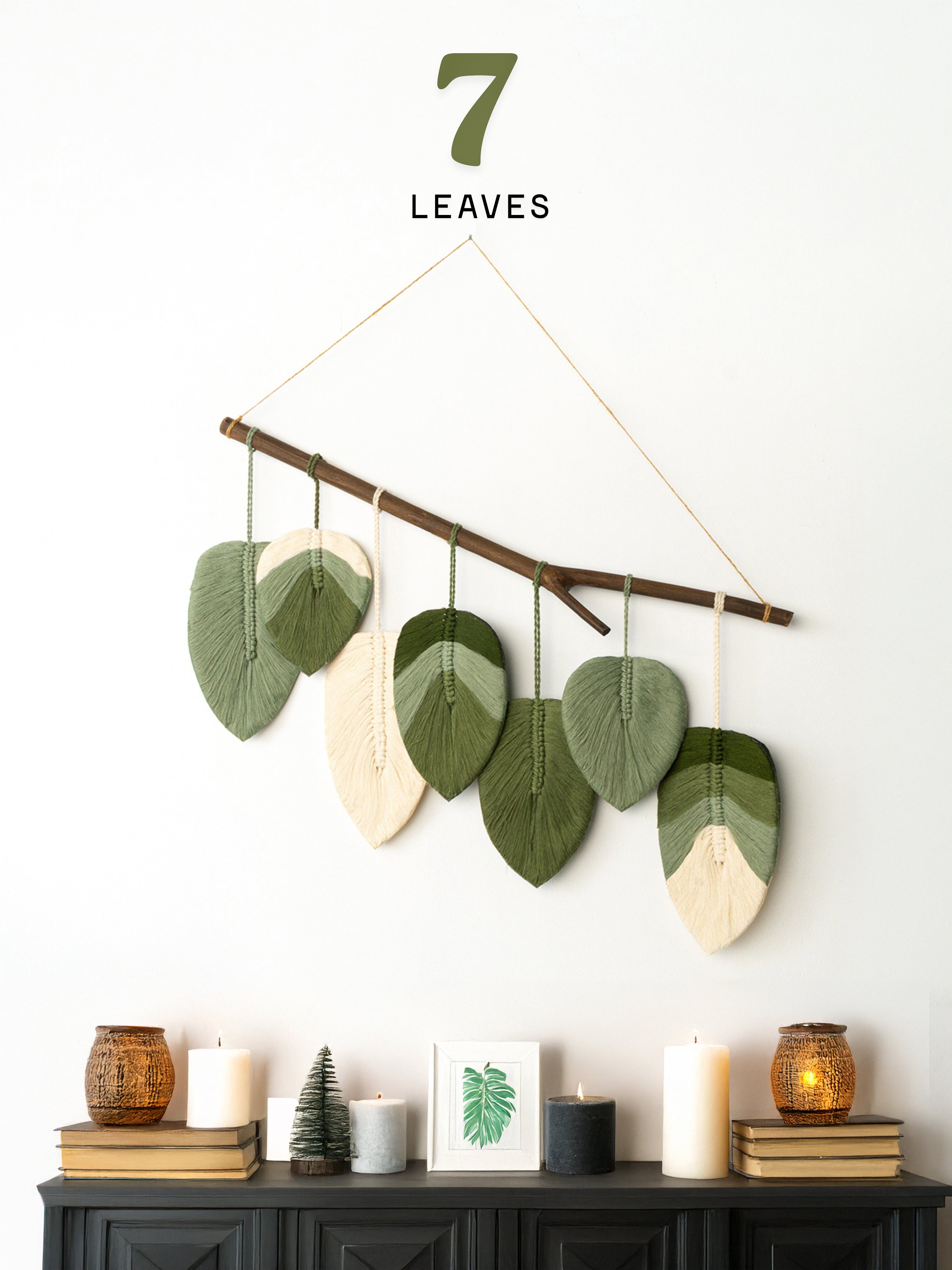 Decorative wall hanging with leaf-shaped leaves on a branch against a white wall.