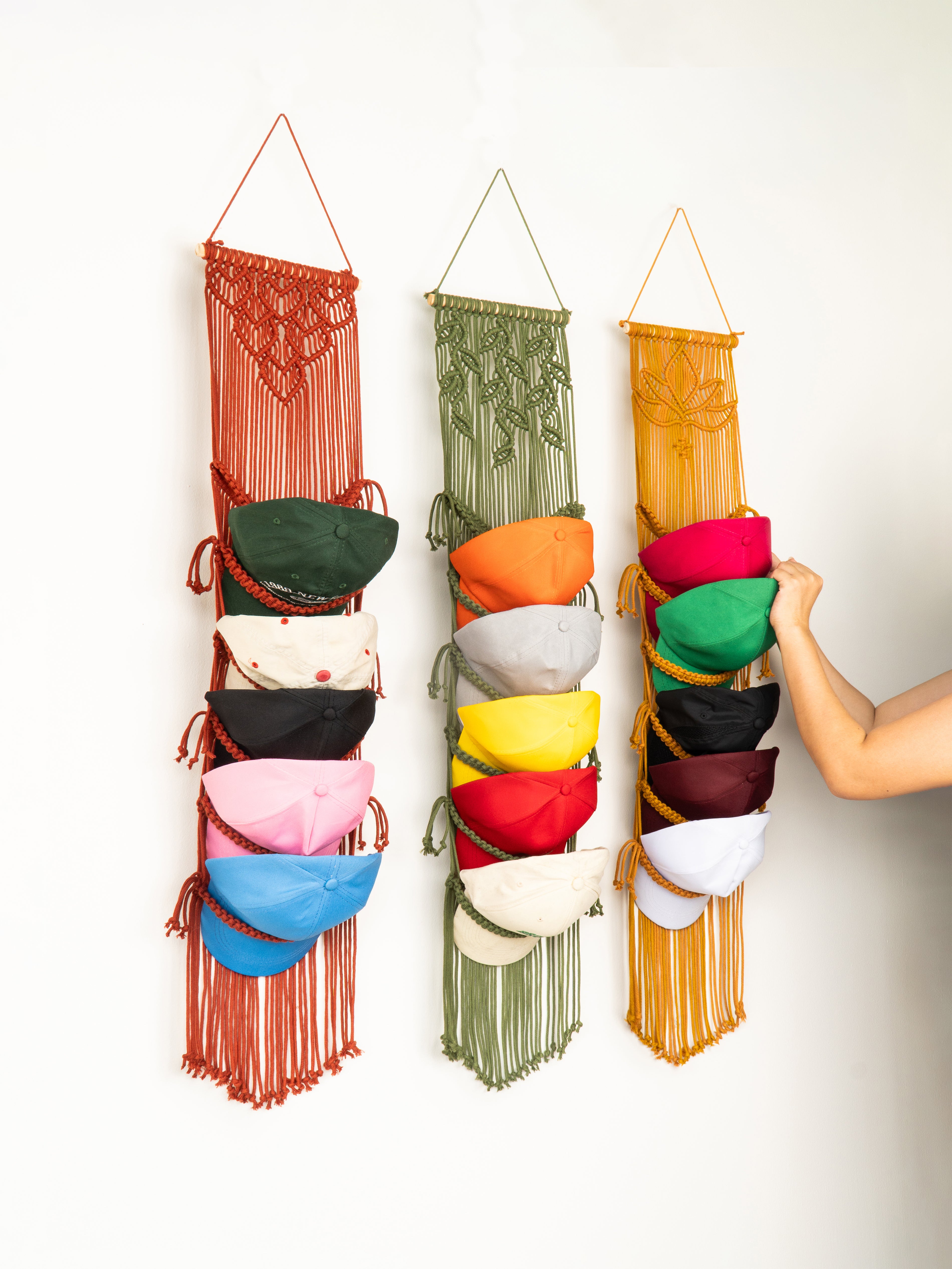 Three colorful macrame wall hangings with various colored bags hanging from them against a white background.