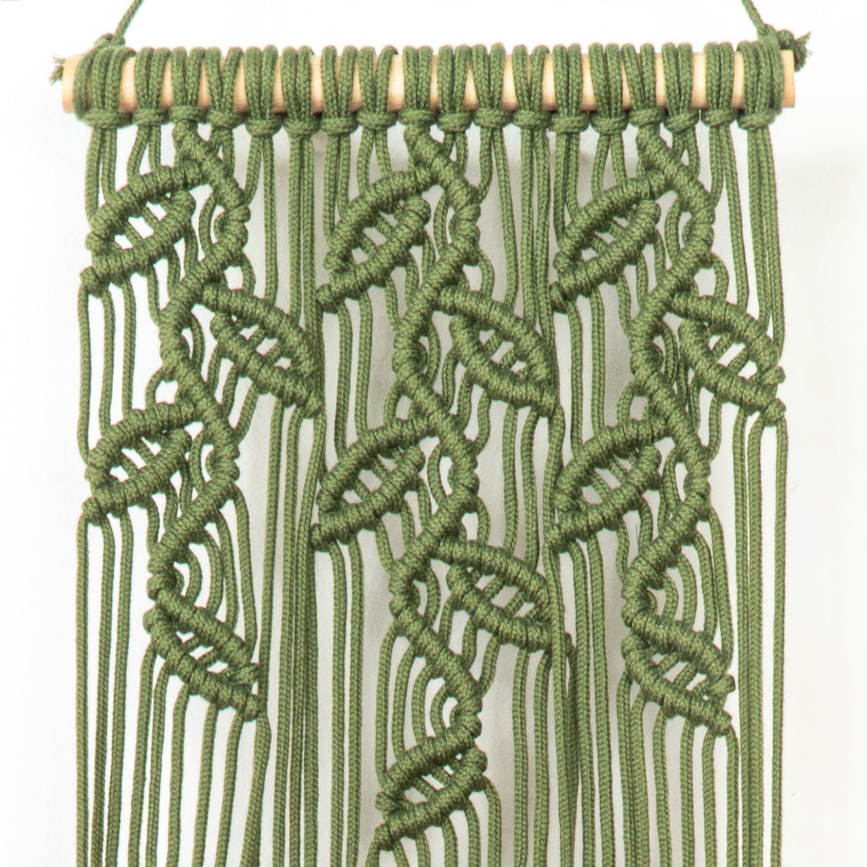 Green macrame wall hanging with a white background